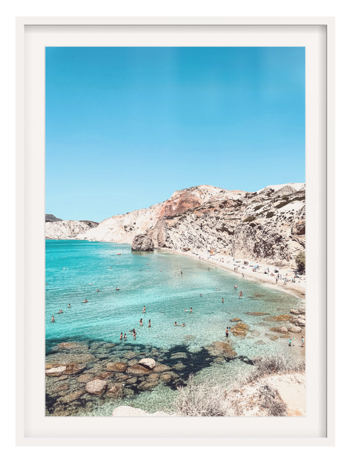 Beach scene with clear blue water and rocky shore, framed in white.