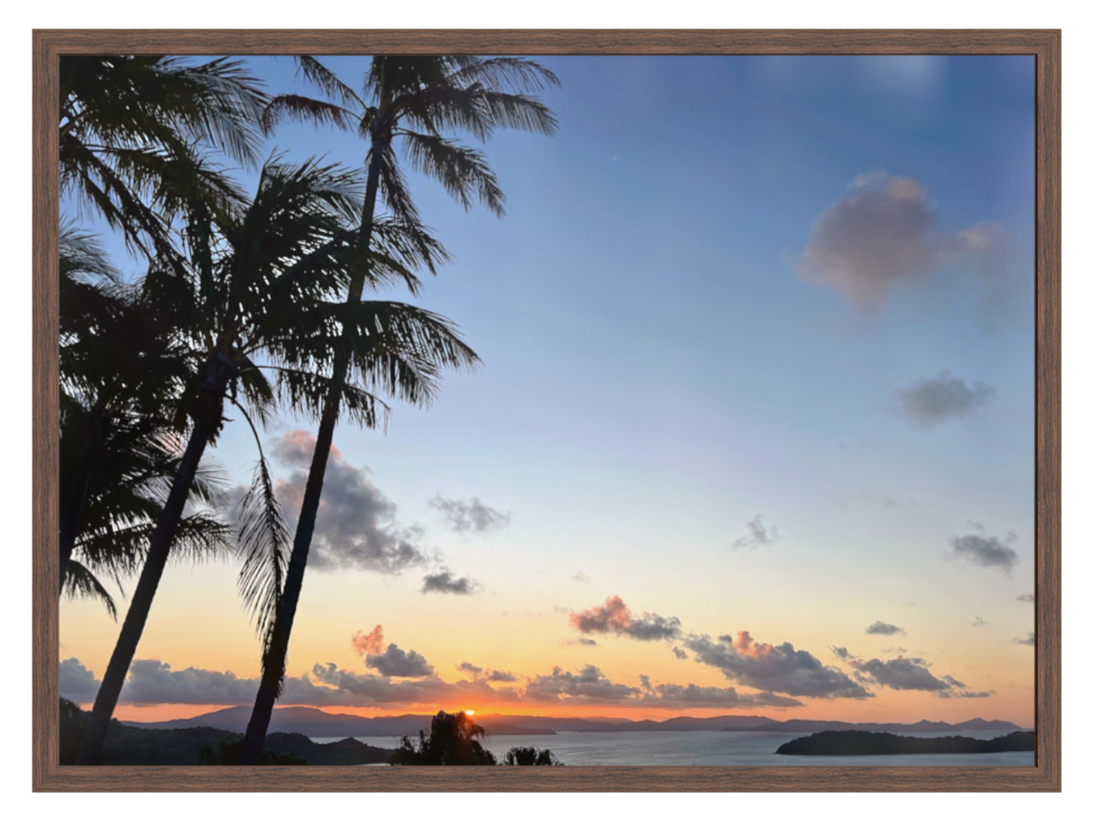 Sunset over a tropical beach with palm trees and a wooden frame.