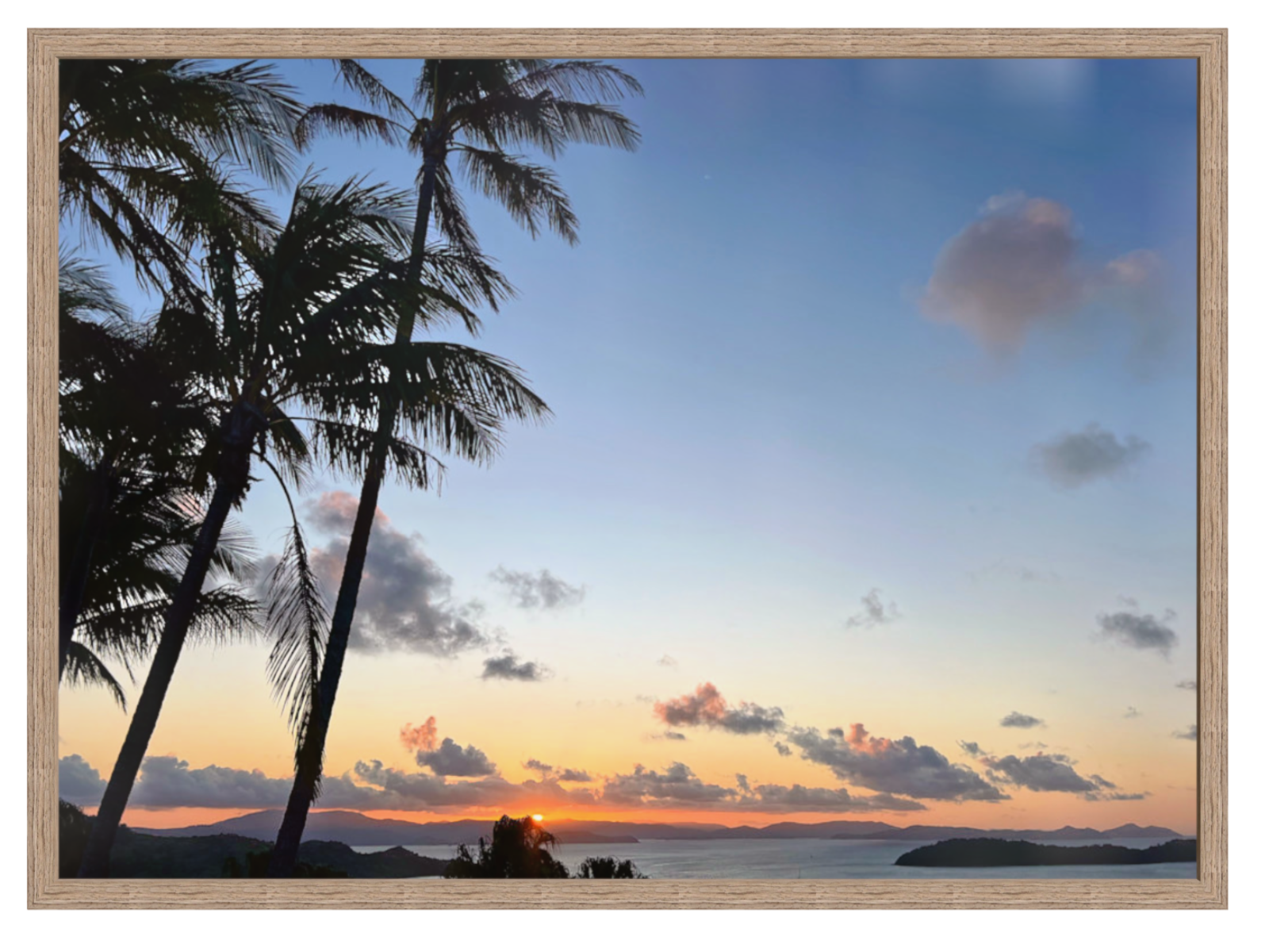 Sunset over a tropical beach with palm trees and mountains in the distance.