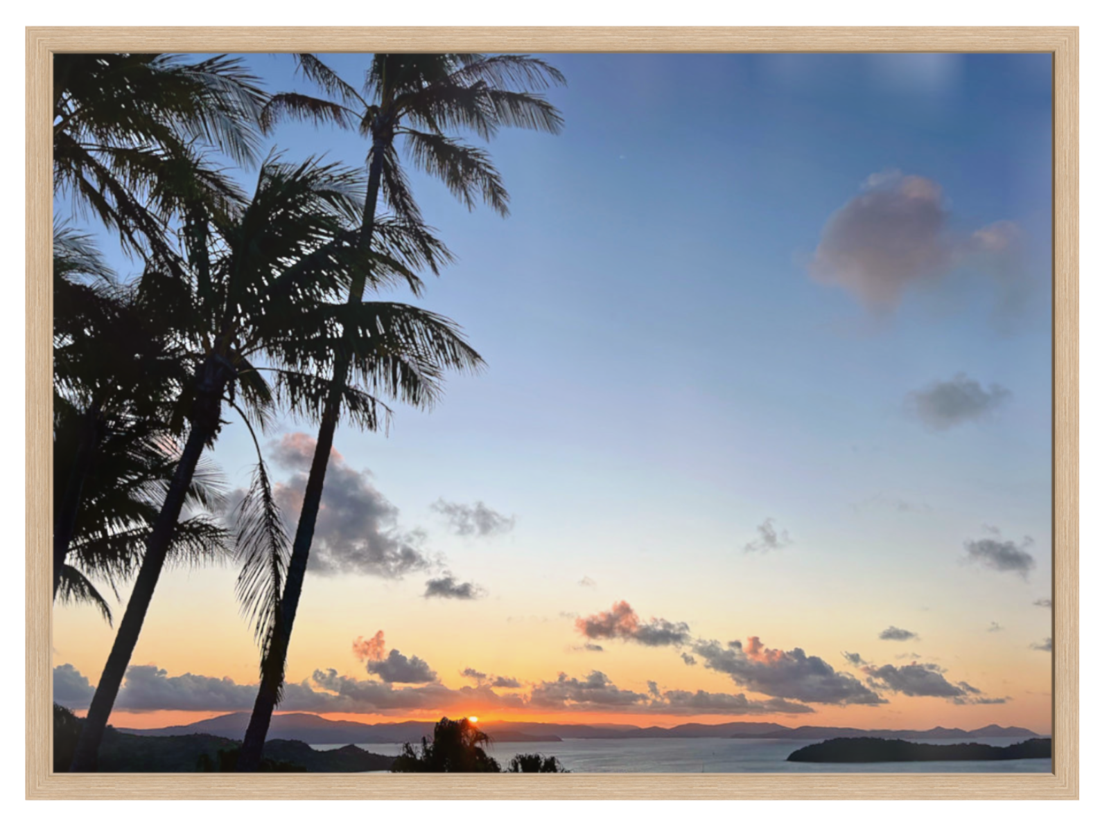 Sunset over a tropical landscape with palm trees and distant mountains.