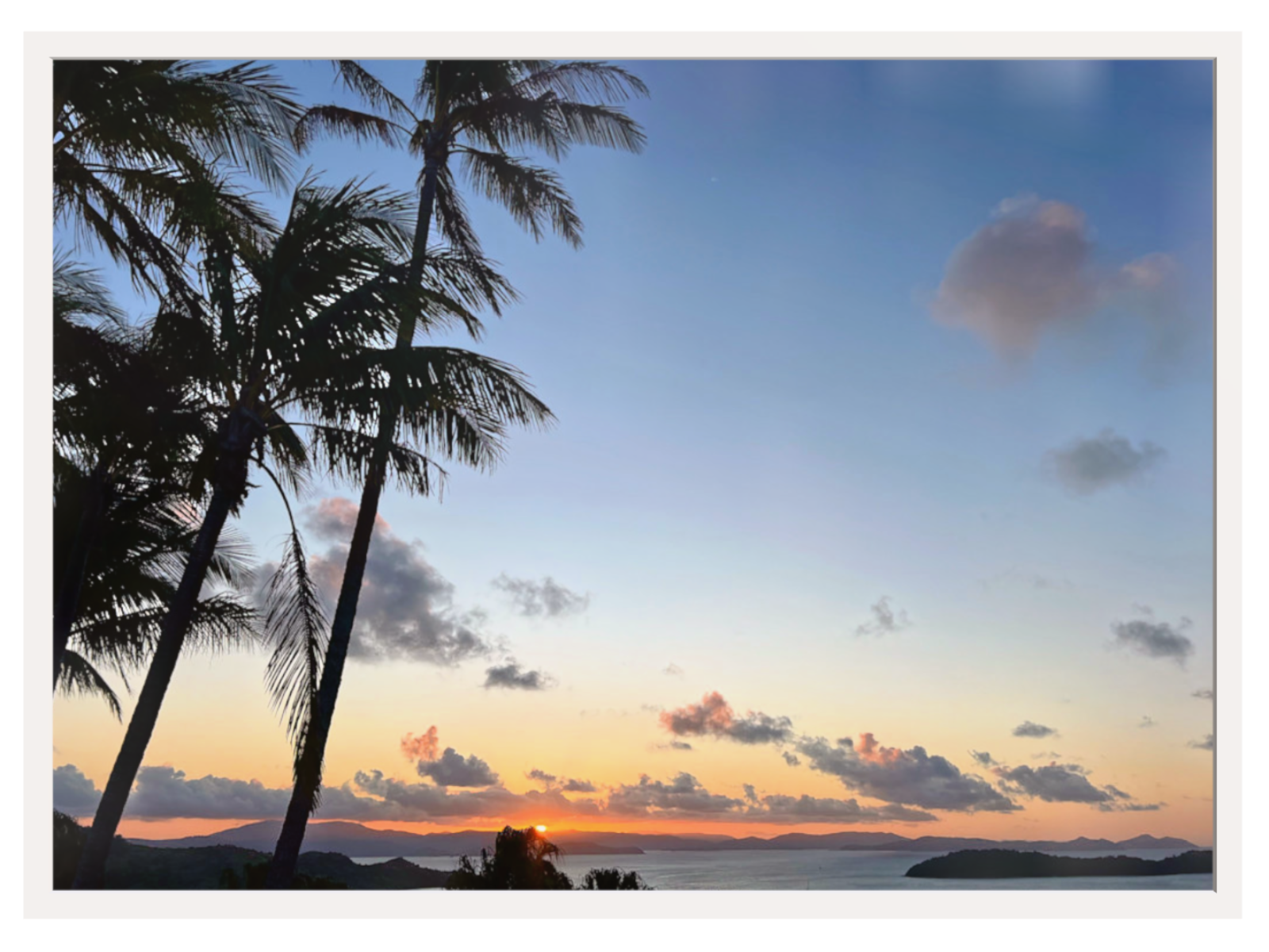 Sunset over a tropical landscape with palm trees and a clear sky.