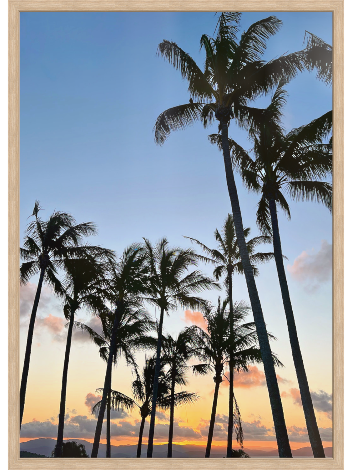 Silhouettes of palm trees against a colorful sunset sky with a wooden frame.