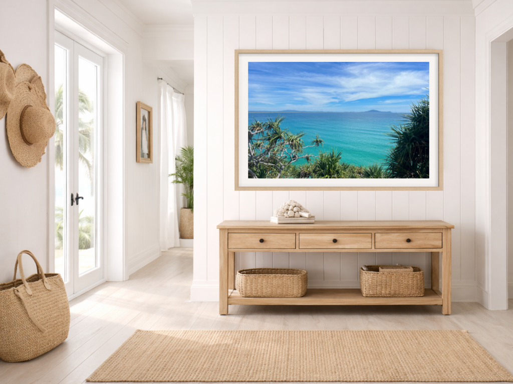 Framed artwork of a beach scene above a wooden console table in a room with white walls and a rug.