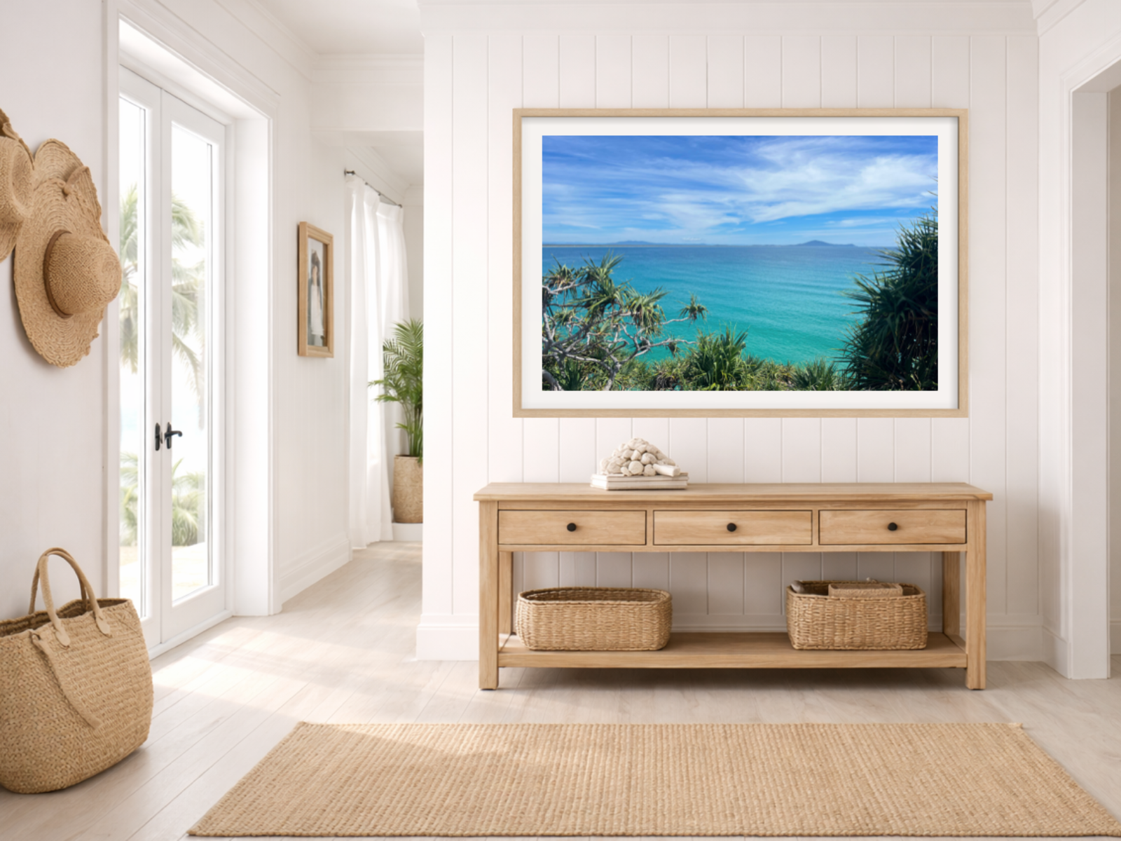 Framed artwork of a beach scene above a wooden console table in a room with white walls and a rug.