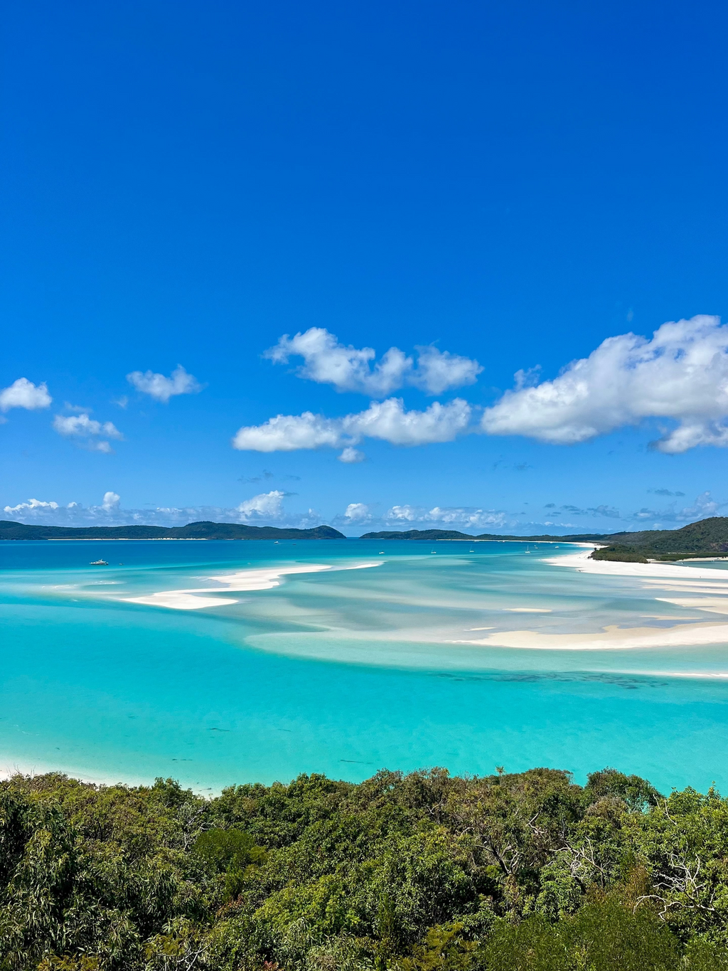 Turquoise waters and white sand beach with blue sky and green trees