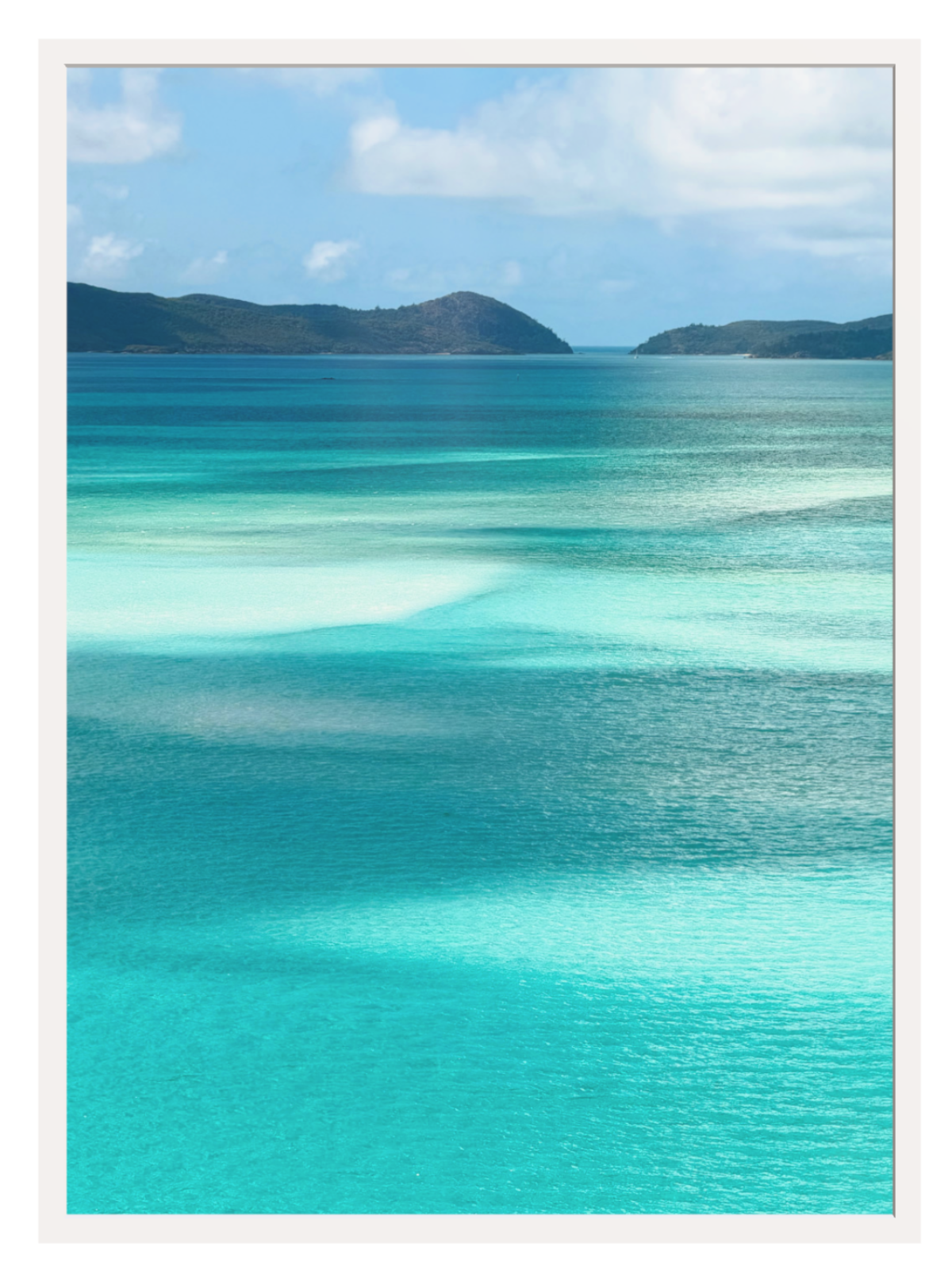 Scenic view of turquoise ocean water with shallow clear pools, distant dark green hills, and a blue sky with white clouds.