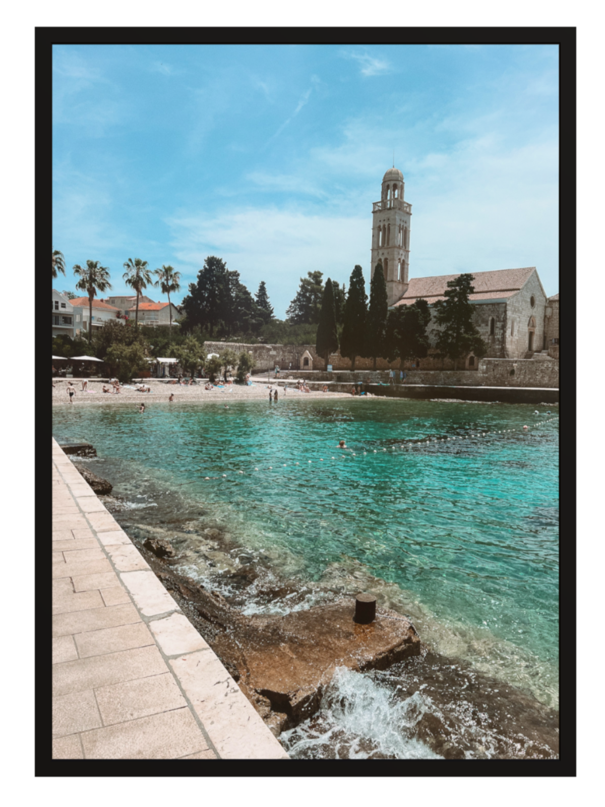 Coastal scene with clear blue water, a beach, and a building with a clock tower.