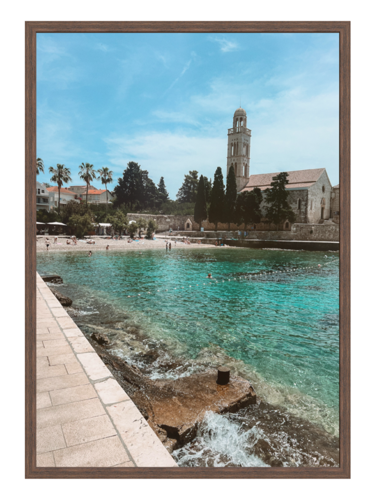 Coastal scene with a church tower, beach, and clear blue water framed in brown.