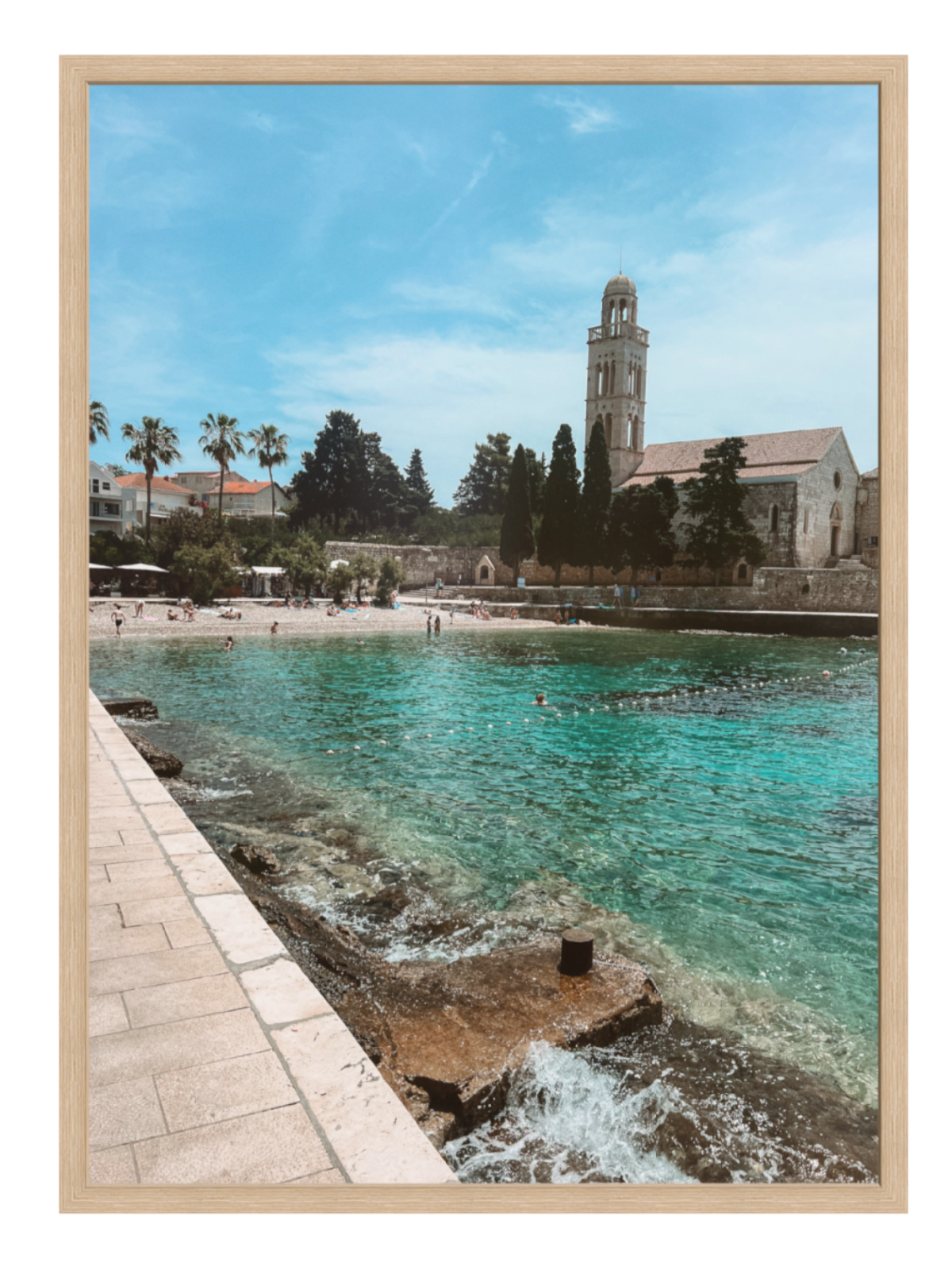 Framed artwork of a coastal scene with a church tower and clear blue water.