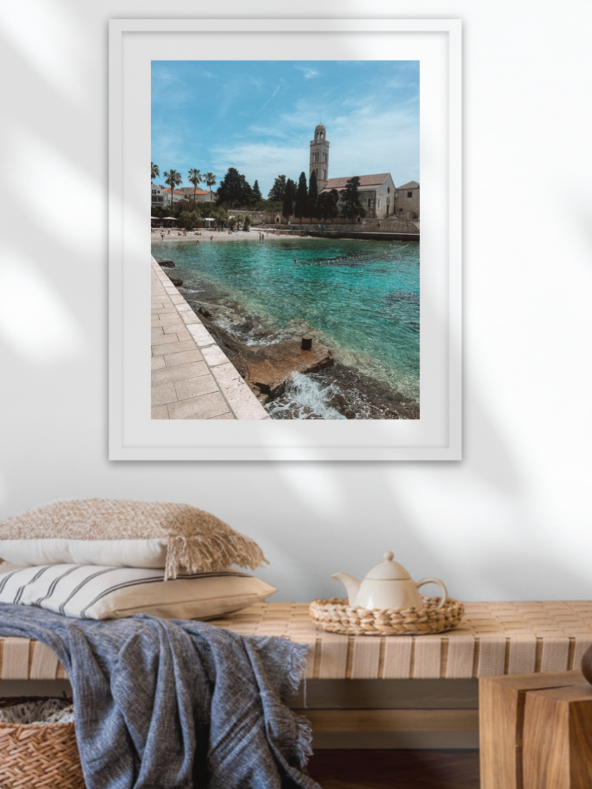 Framed artwork of a coastal scene above a wooden bench with decorative items.