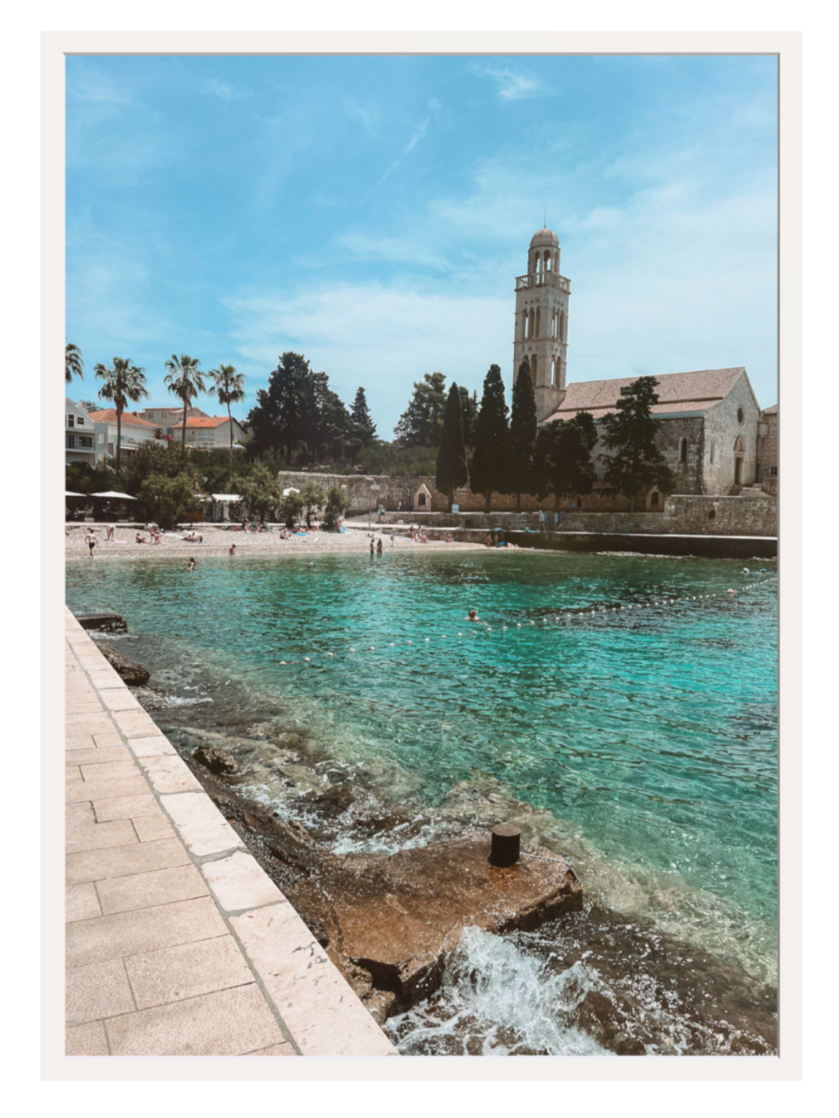 Coastal scene with clear blue water, a beach, and a building with a clock tower.