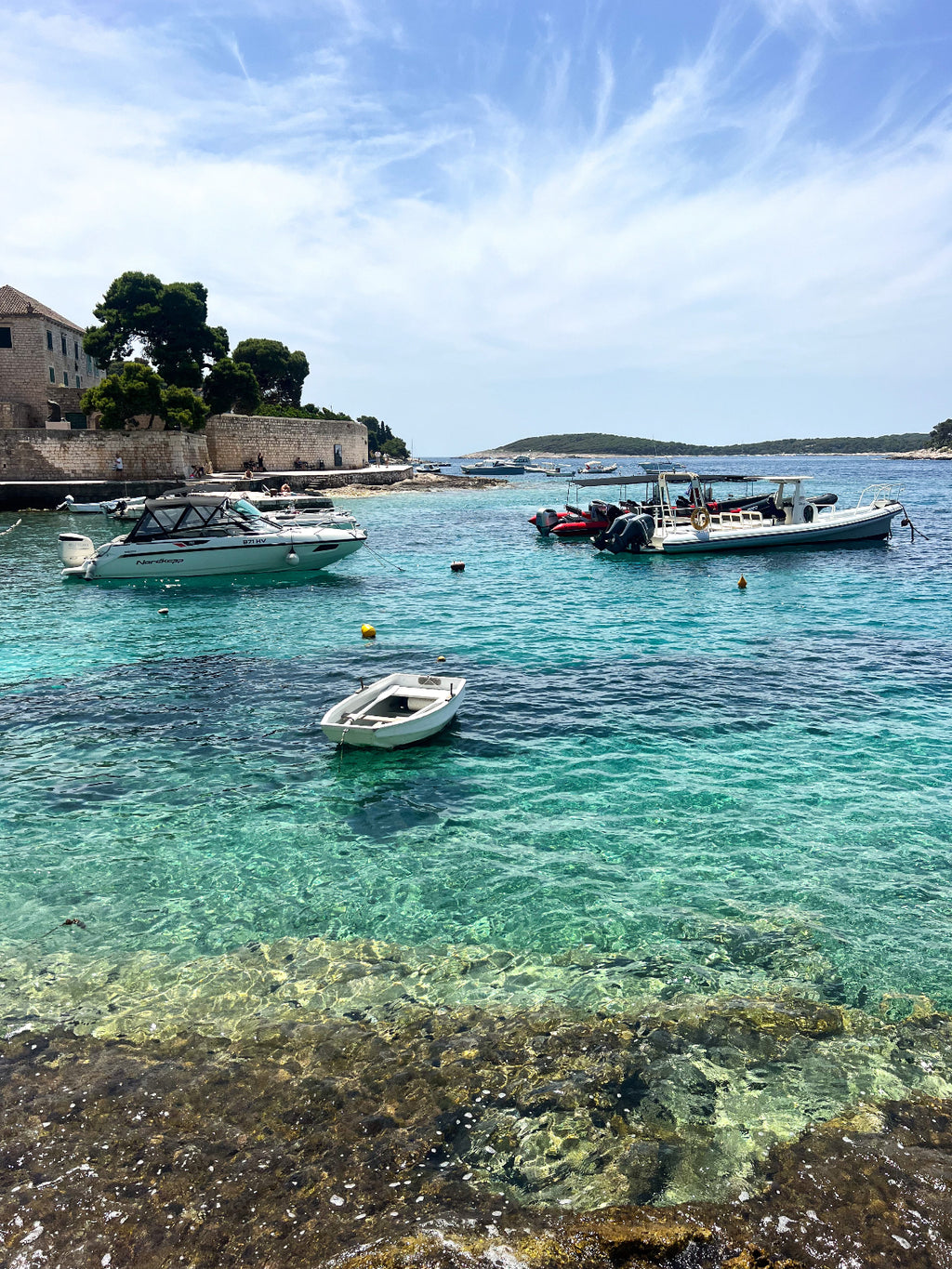 Boats in a harbor with clear blue water and a building in the background