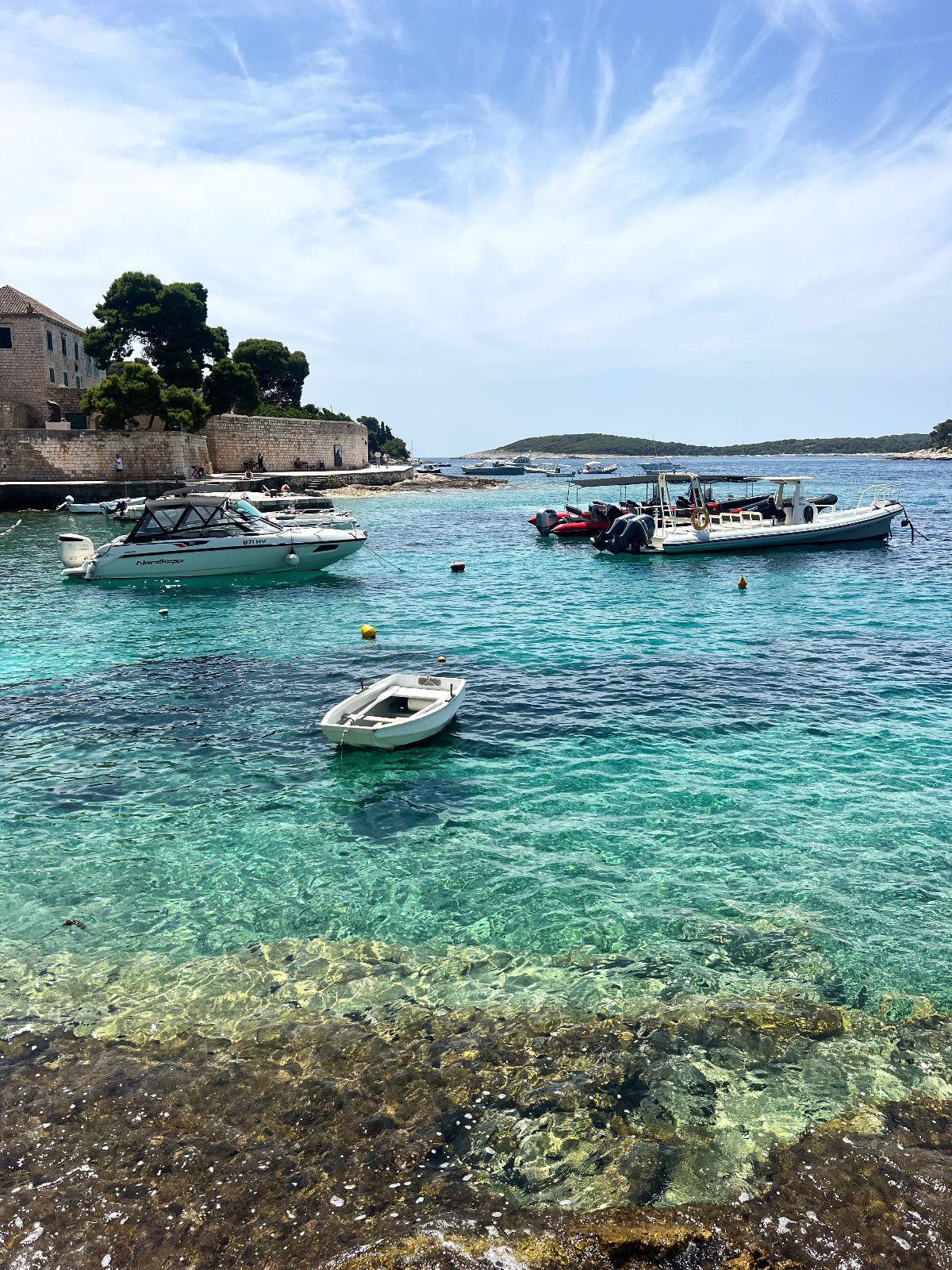 Boats in a harbor with clear blue water and a building in the background