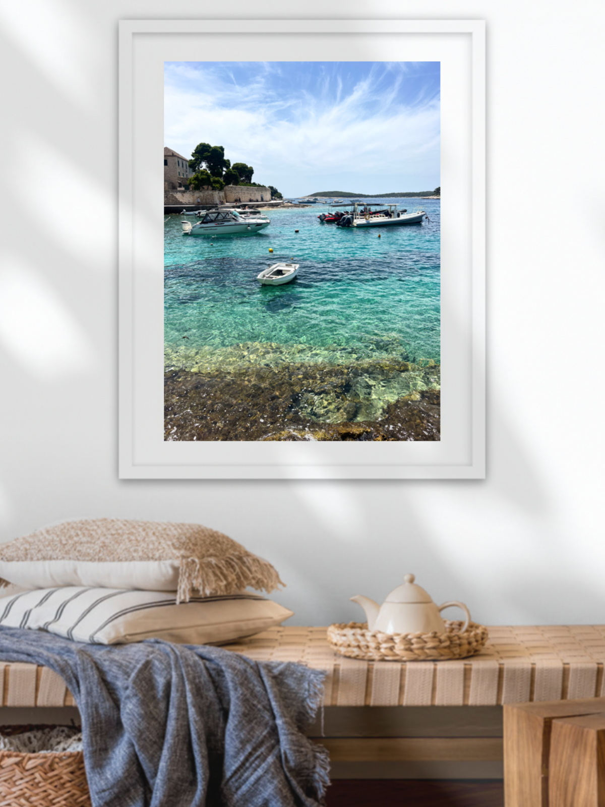 Framed photograph of a coastal scene with boats on a wall above a wooden bench.