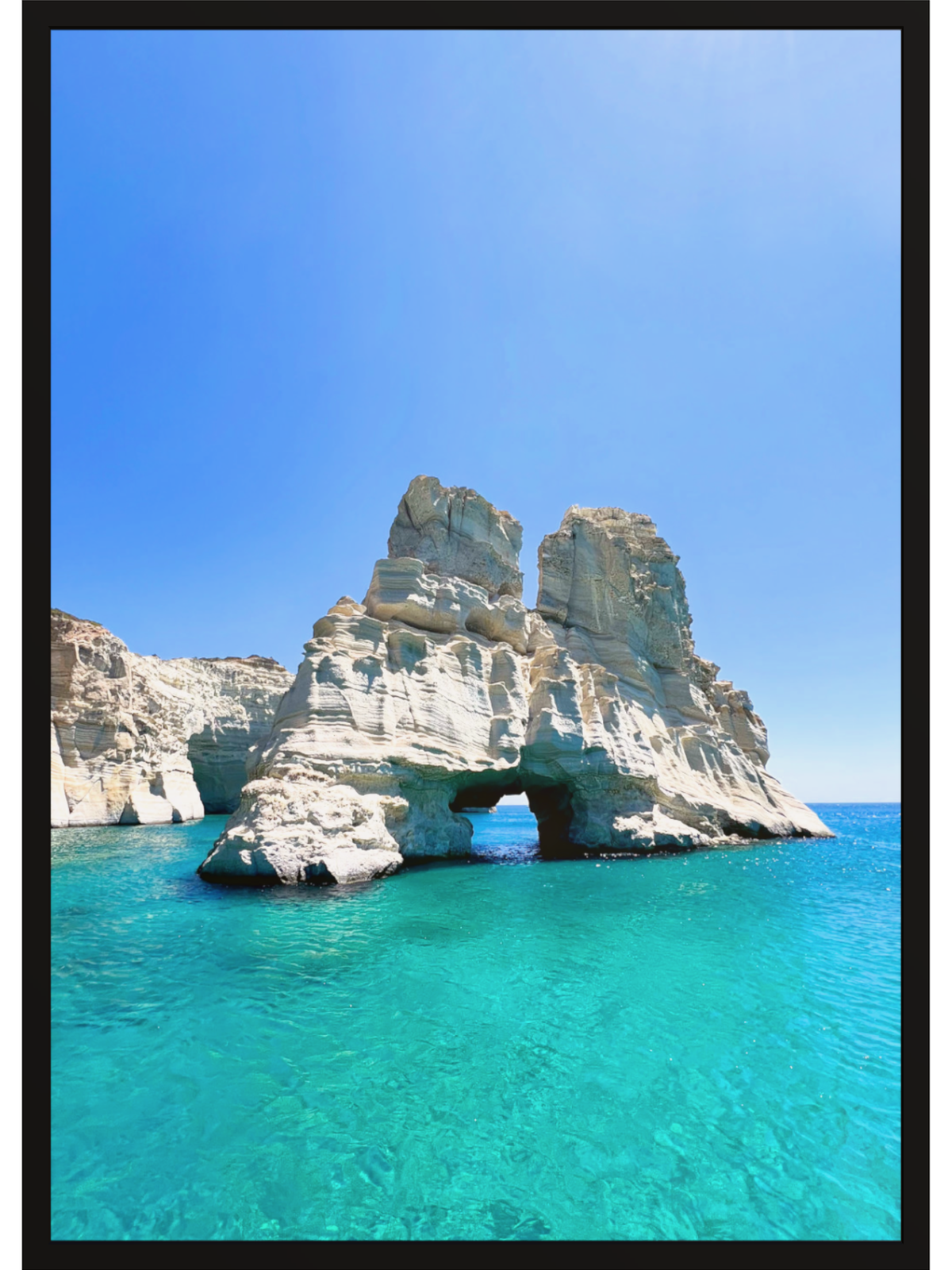 Rock formation with a natural arch over turquoise water under a clear blue sky.