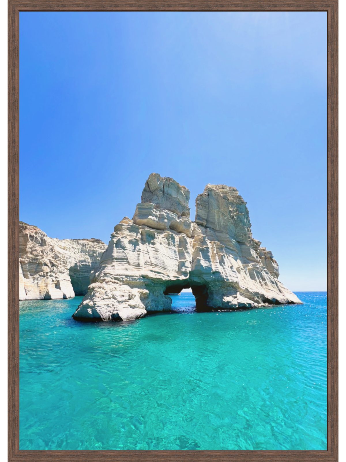 Rock formation with a natural arch in clear blue water under a bright blue sky.