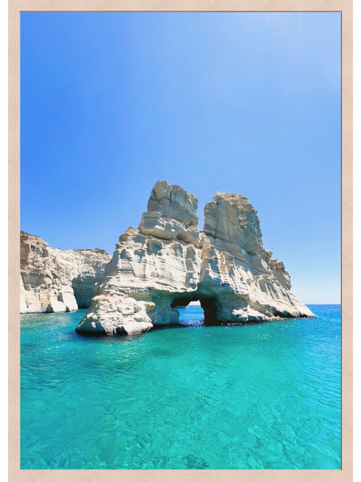 Rock formation with a natural arch in clear blue water under a bright blue sky.