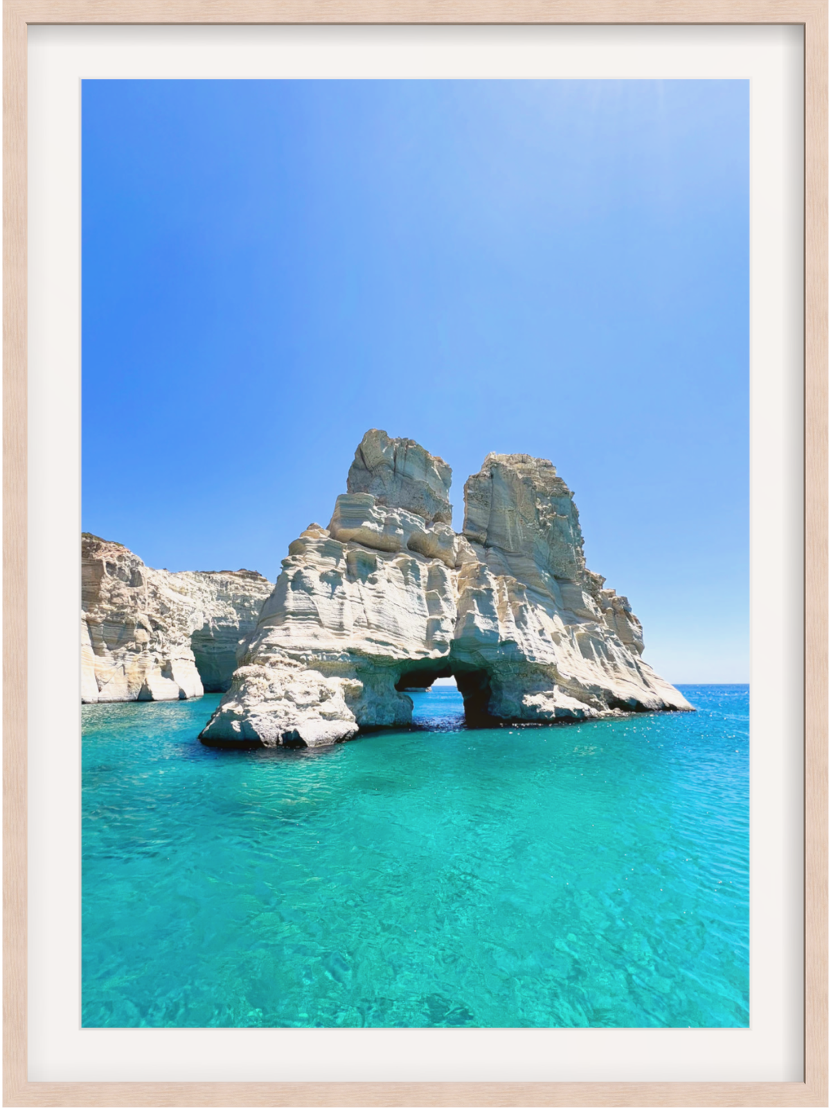 Rock formation with a natural arch in clear blue water under a bright blue sky.