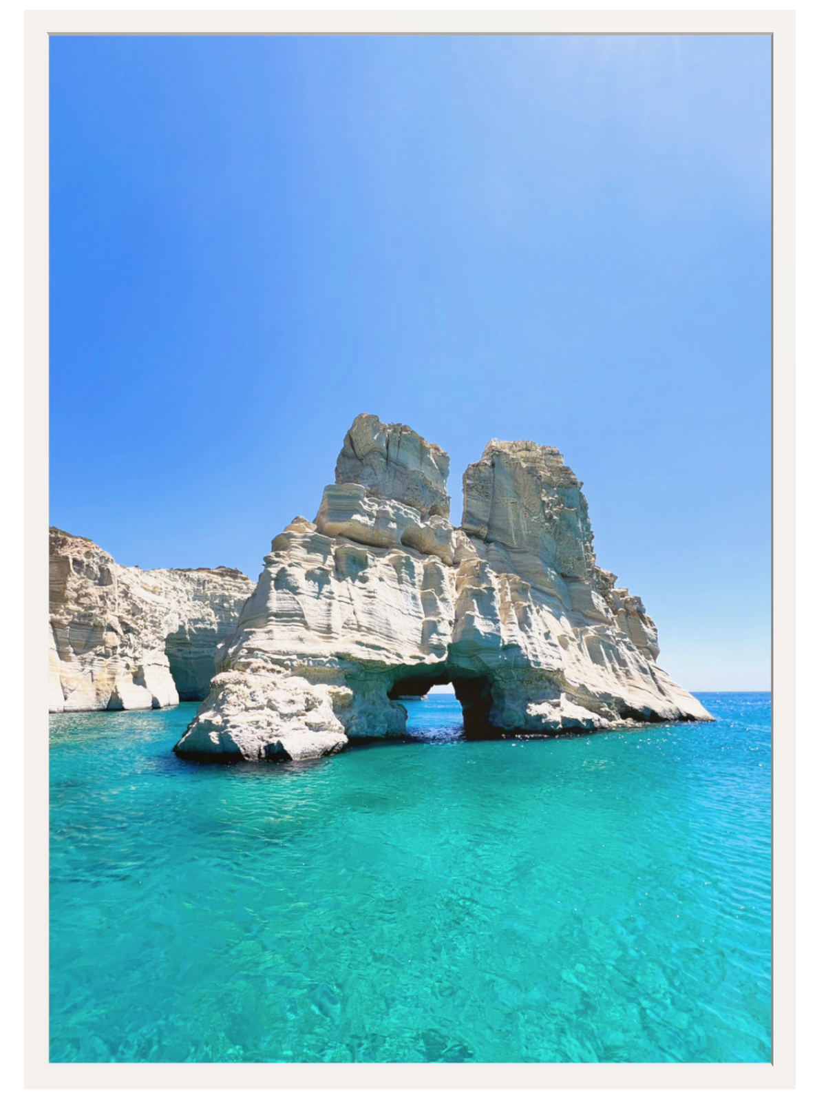 Rock formation with a natural arch over clear blue water under a bright blue sky.