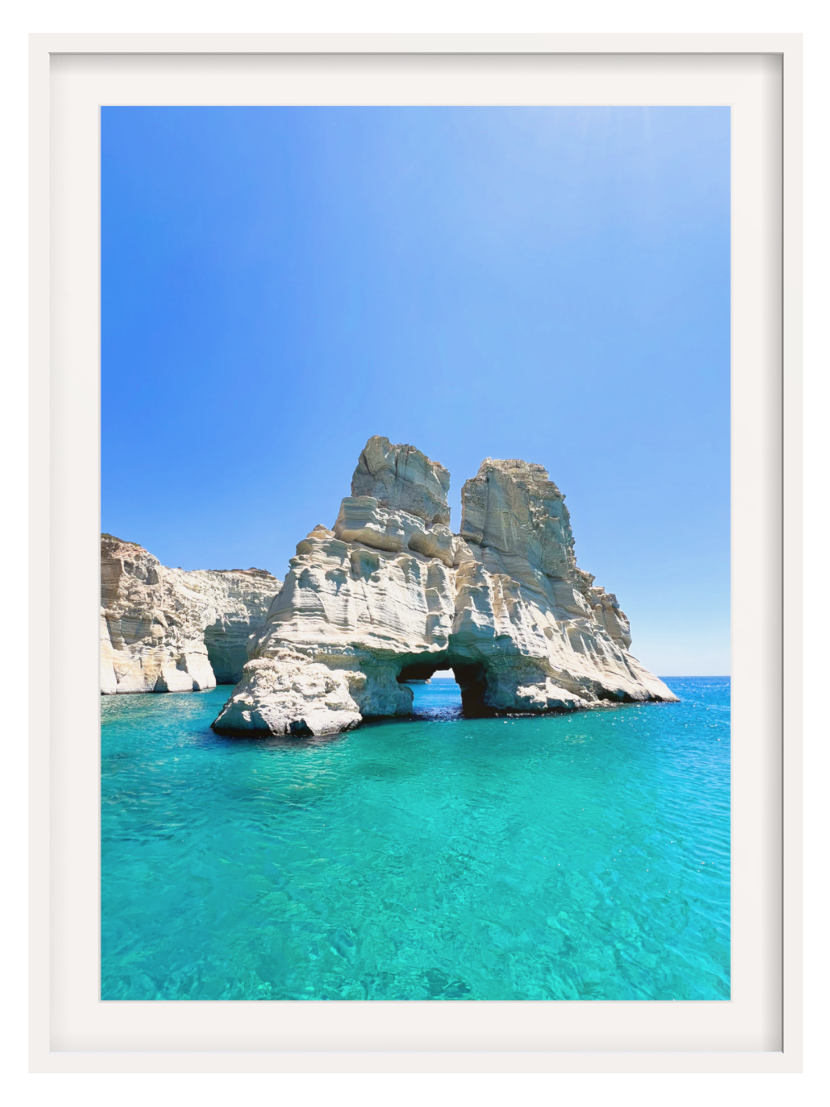 Rock formation with a natural arch in clear blue water under a bright blue sky.