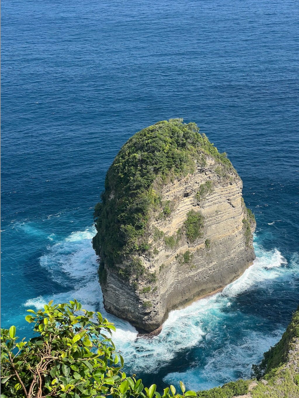 Isolated rock formation in the middle of a body of water with clear blue sky.