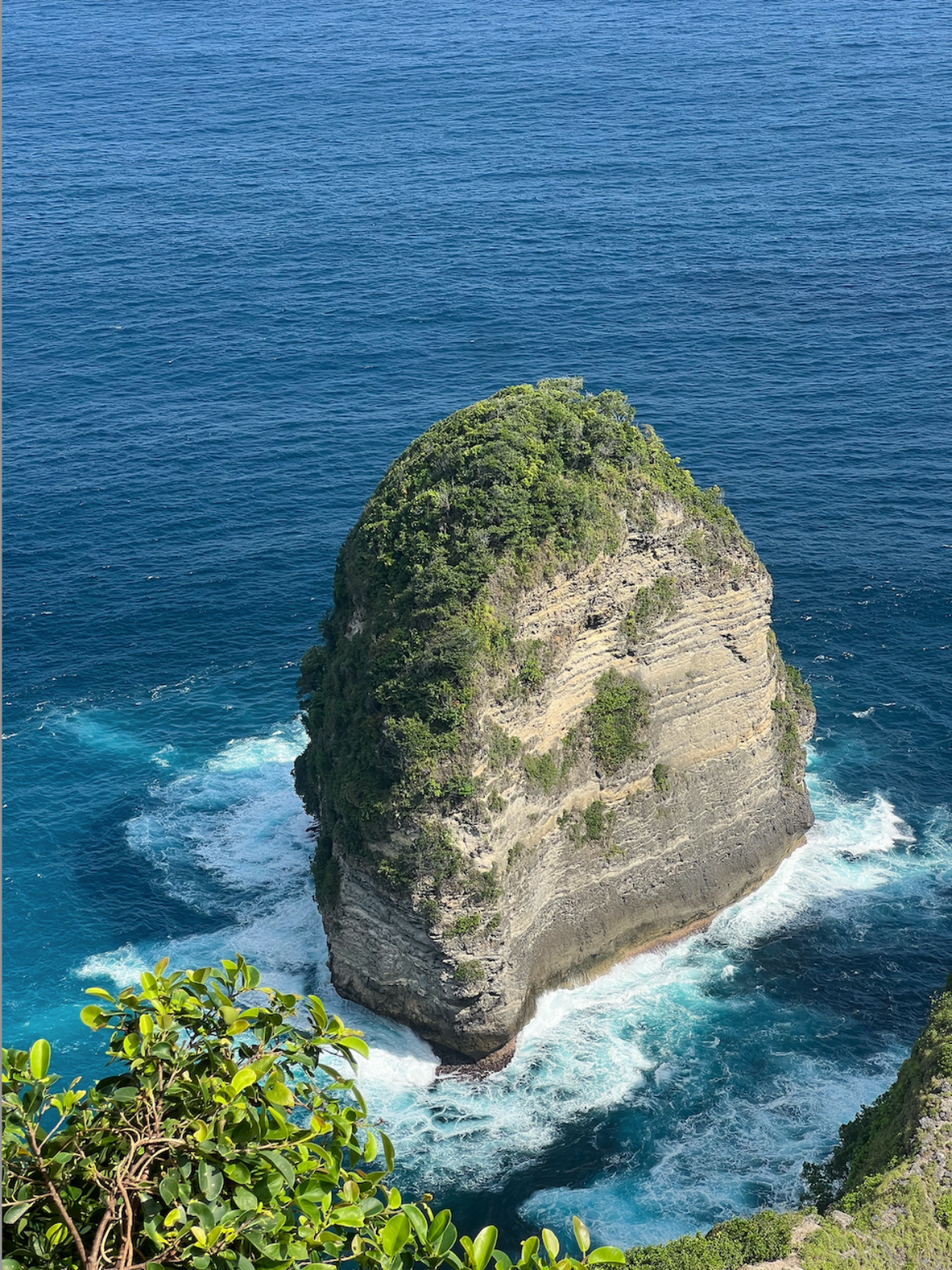 Isolated rock formation in the middle of a body of water with clear blue sky.