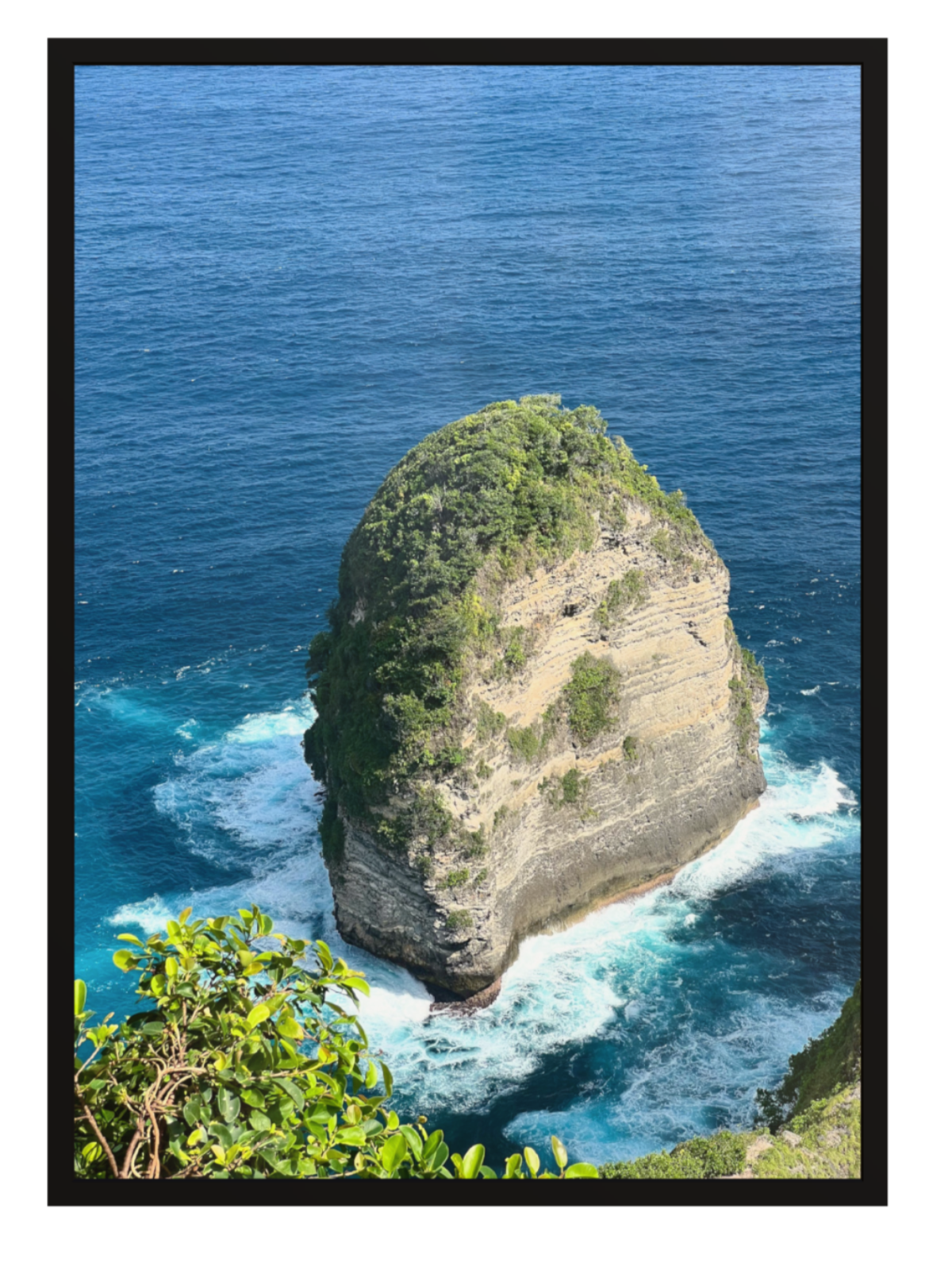 Black Frame Isolated rock formation in the middle of the ocean with a clear blue sky.