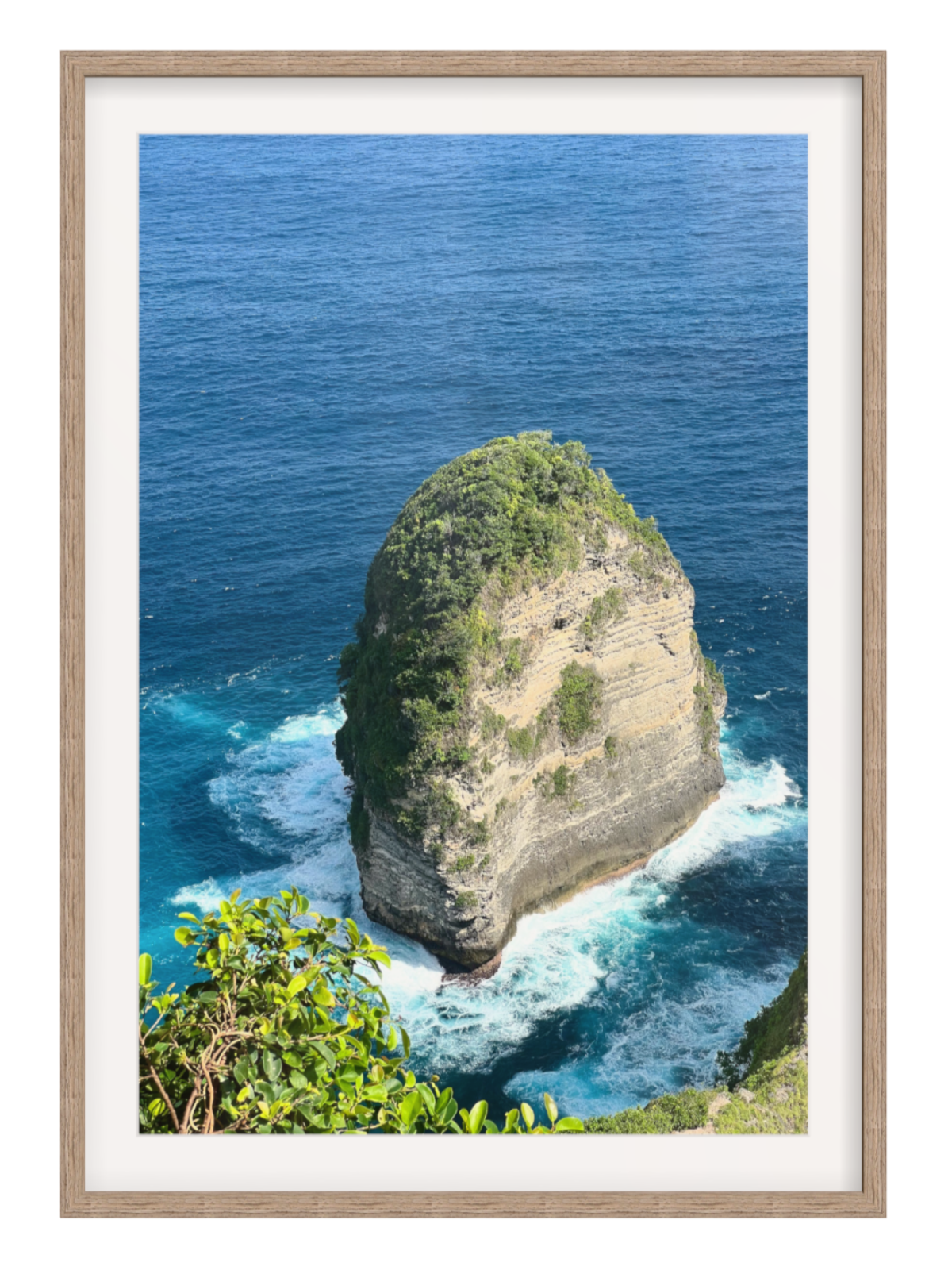 Hazel Framed photograph of a rocky island with ocean waves, framed in a light wood color.