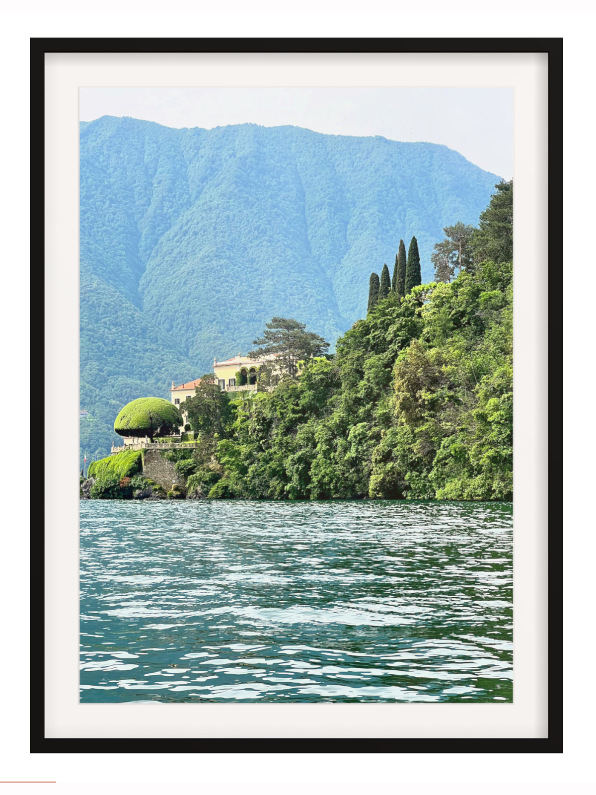 Framed photograph of a scenic view with mountains, trees, and a house by a lake.