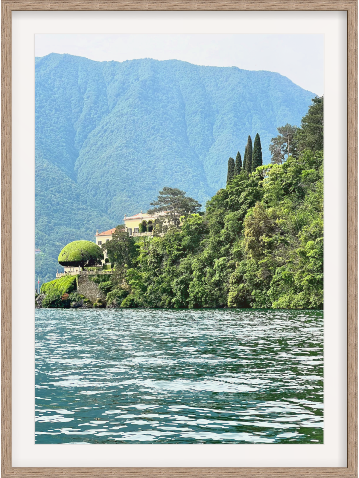 Framed photograph of a scenic landscape with a house on a hill overlooking a lake.