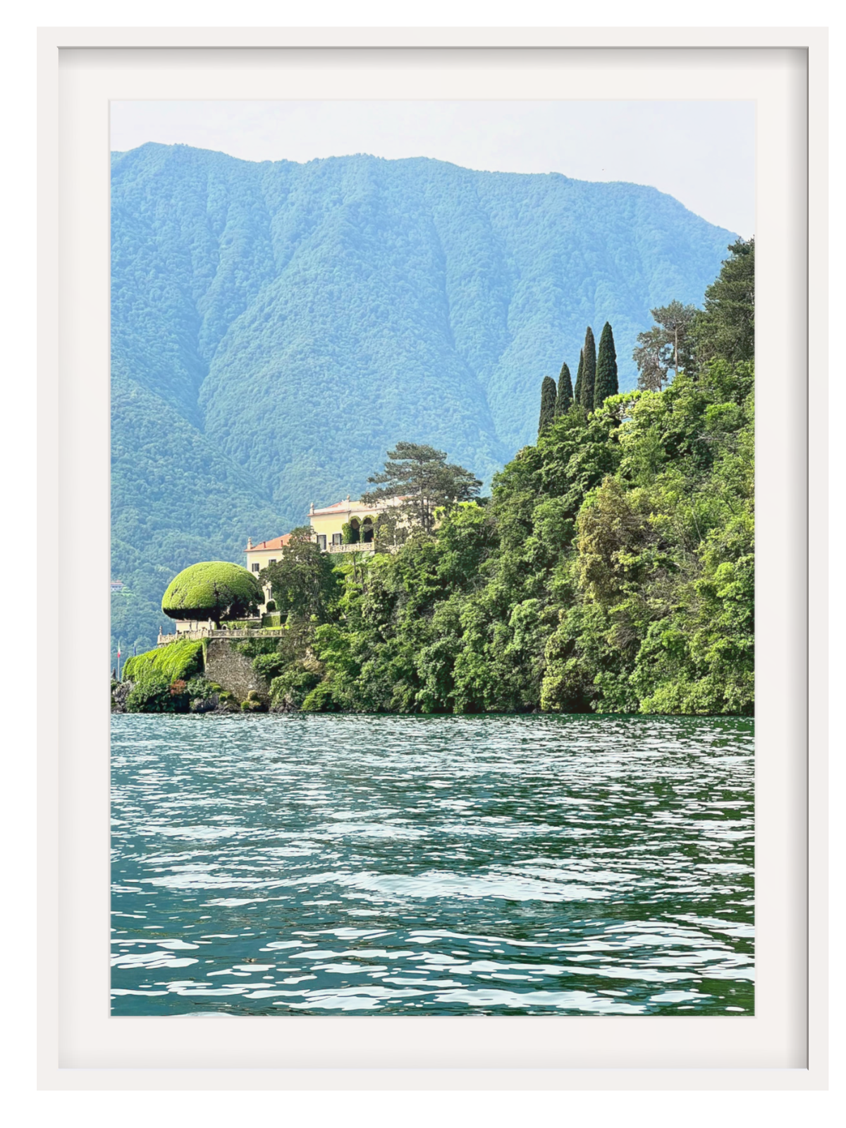 Framed photograph of a scenic landscape with mountains, trees, and a building by a lake.