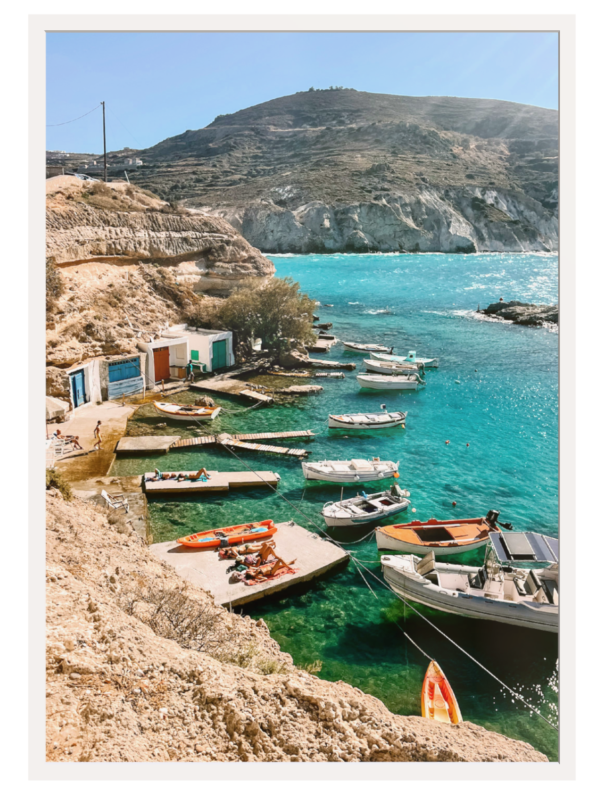 Coastal scene with boats docked in a harbor surrounded by mountains and clear blue water.