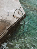 Bottle on a concrete platform with a metal ladder into clear blue water