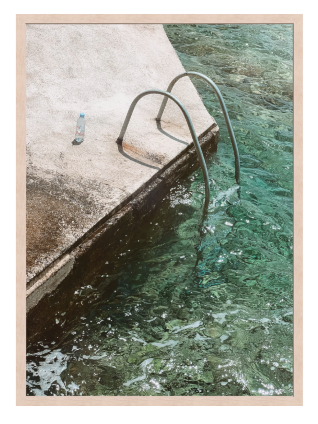 Framed photograph of a pool with a metal ladder and a bottle on the edge.