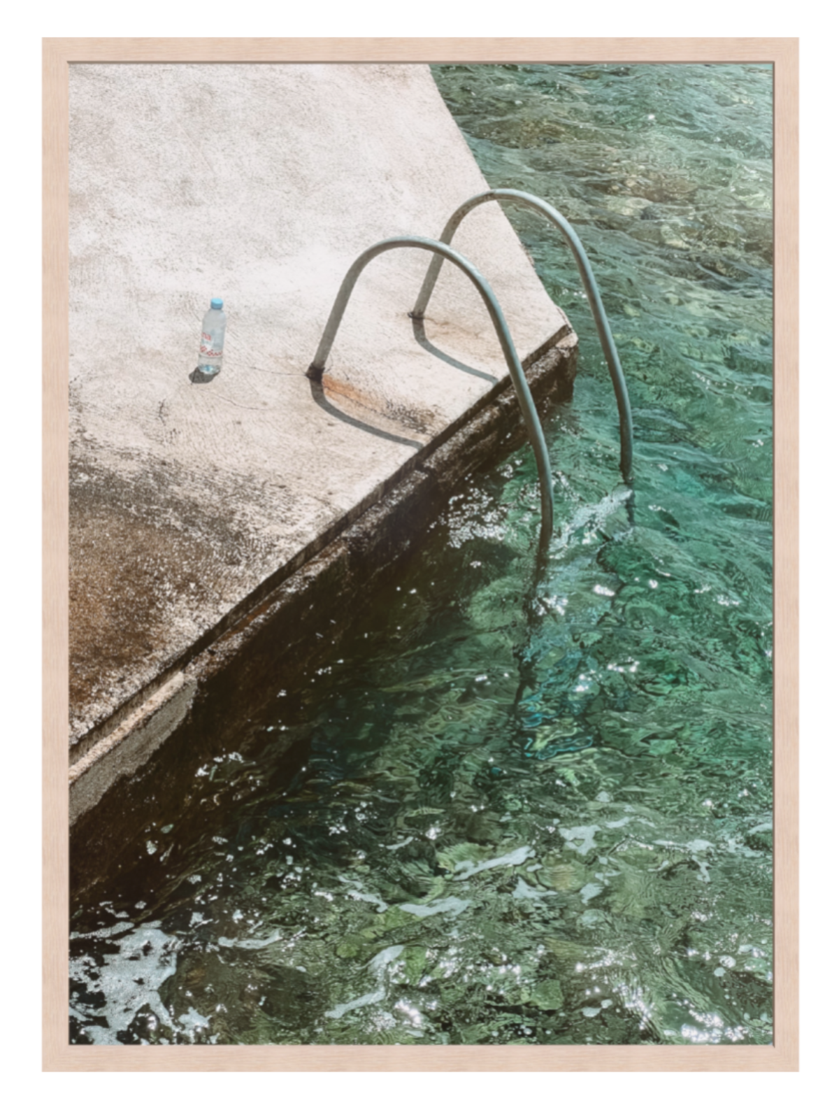 Framed photograph of a pool with a metal ladder and a bottle on the edge.