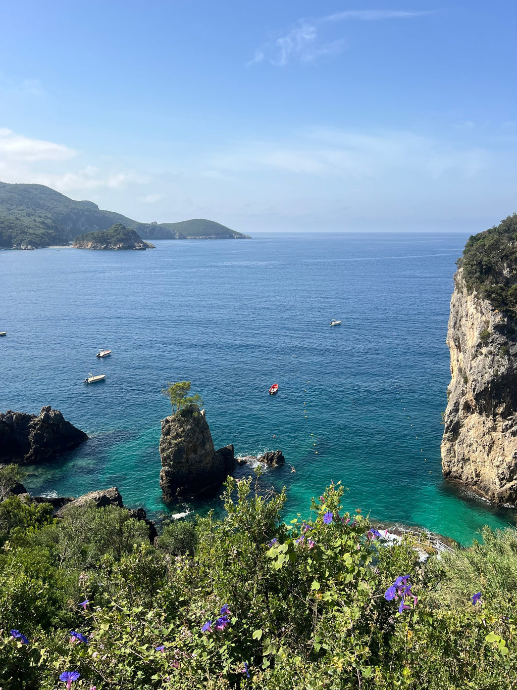 Coastal scene with rocky cliffs, clear blue water, and a few boats.