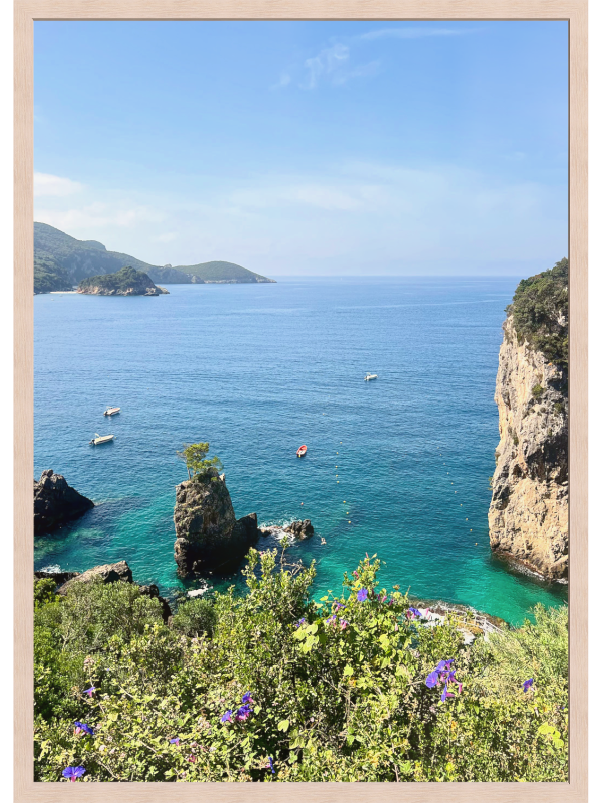 Framed artwork of a coastal scene with clear blue water, rocky cliffs, and greenery.