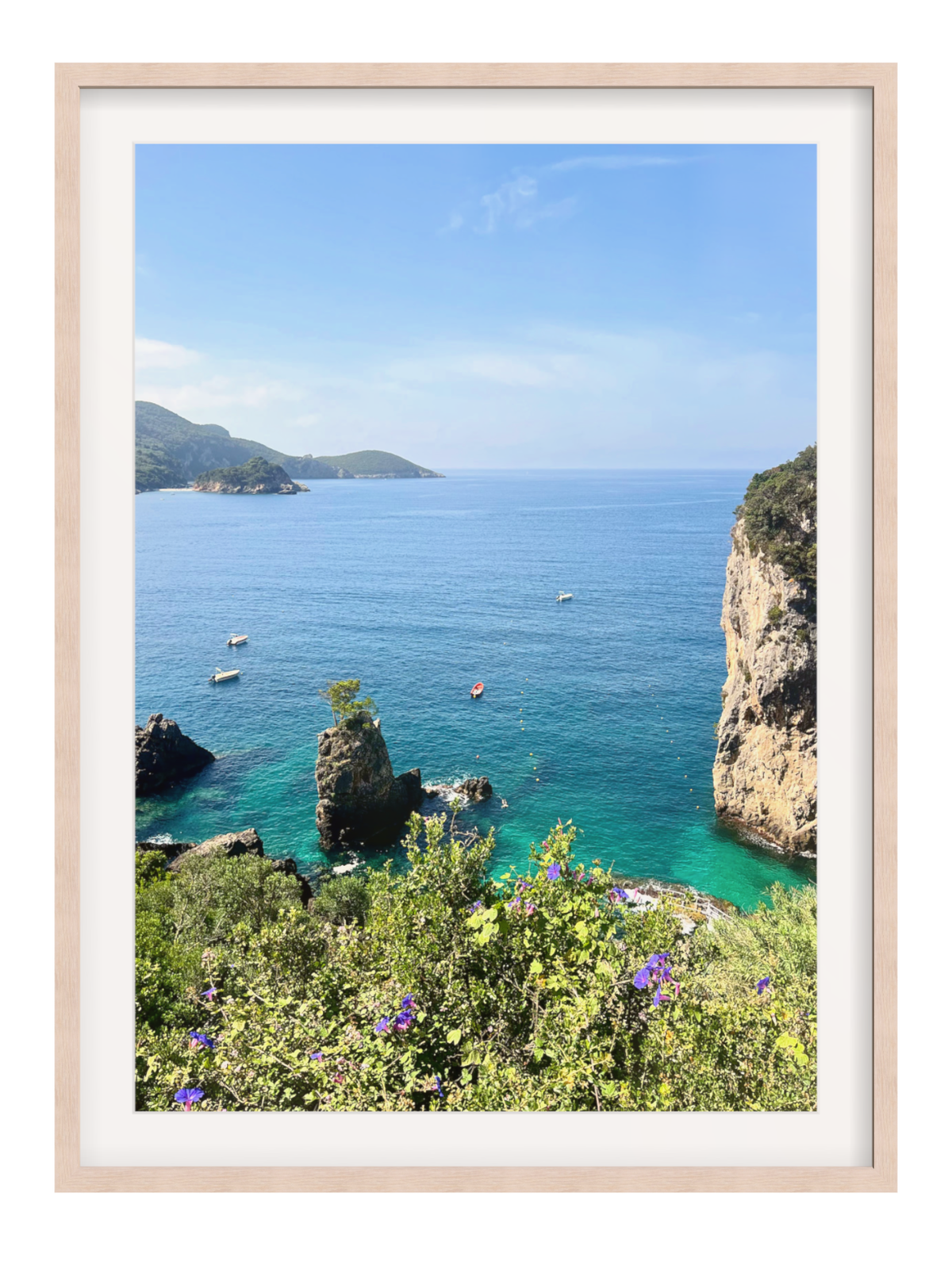 Framed photograph of a coastal landscape with blue sea, green cliffs, and clear sky.