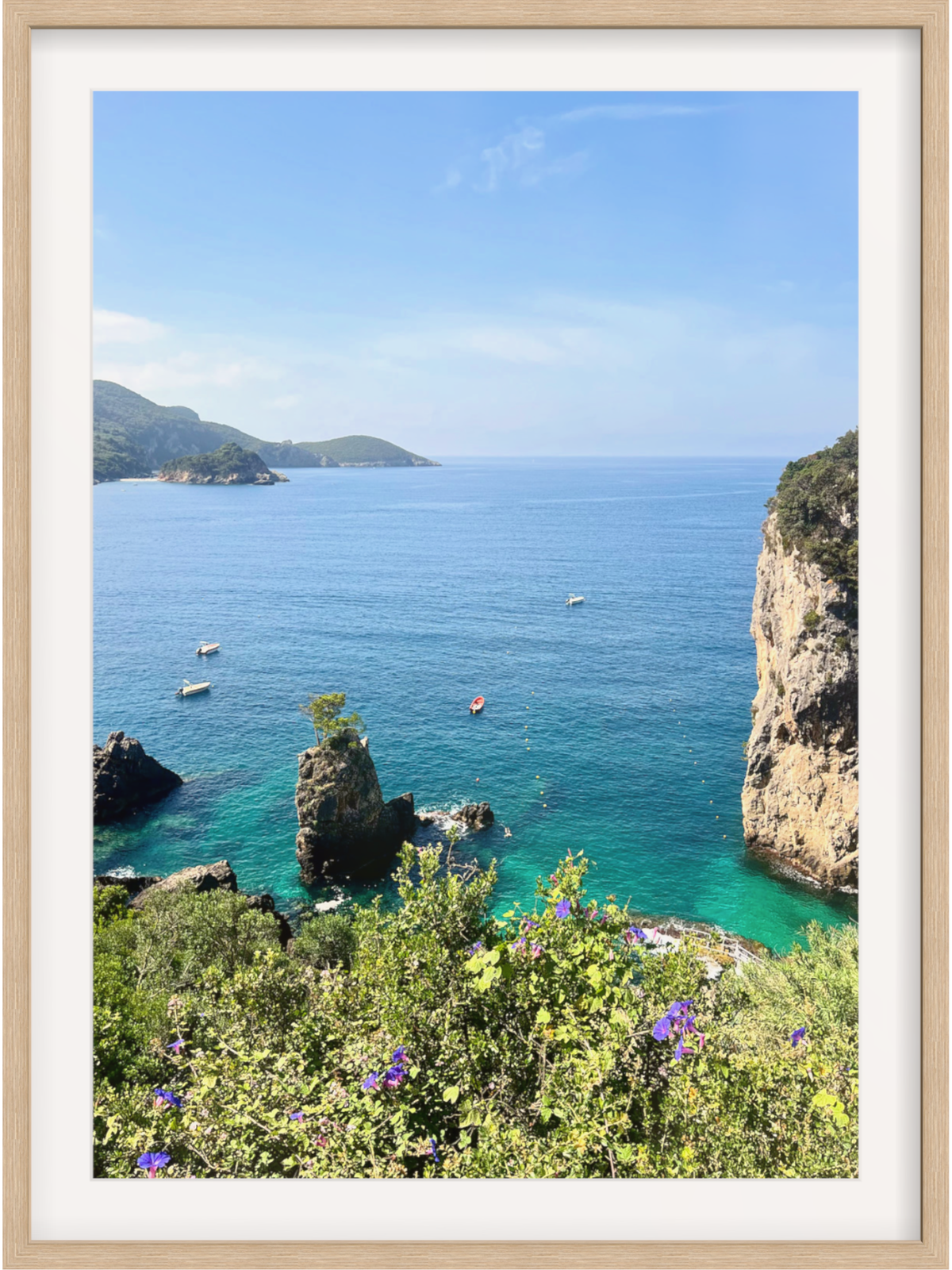 Framed photograph of a coastal landscape with clear blue water, rocky cliffs, and greenery.