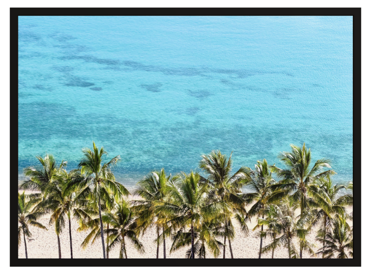 A framed tropical beach scene print featuring a row of green palm trees along a sandy shore, with clear turquoise ocean water filling the background.