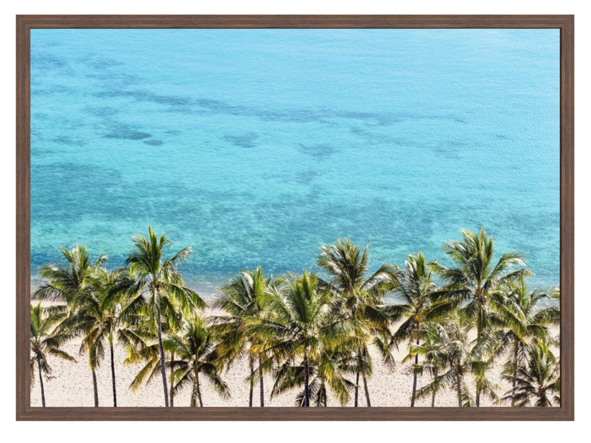 Framed wall art featuring a tropical beach scene with turquoise ocean water, a sandy shore, and a row of green palm trees, shown in a dark brown frame against a white background.