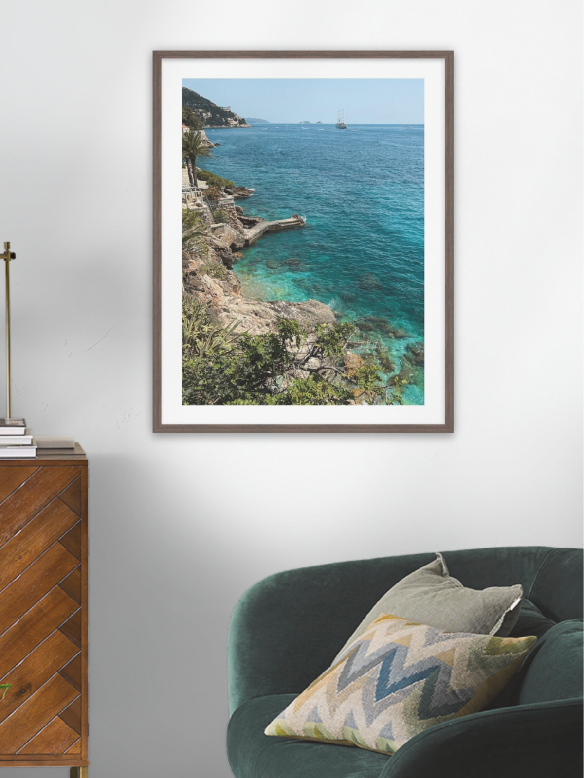 Framed artwork of a coastal scene above a wooden cabinet and green sofa.