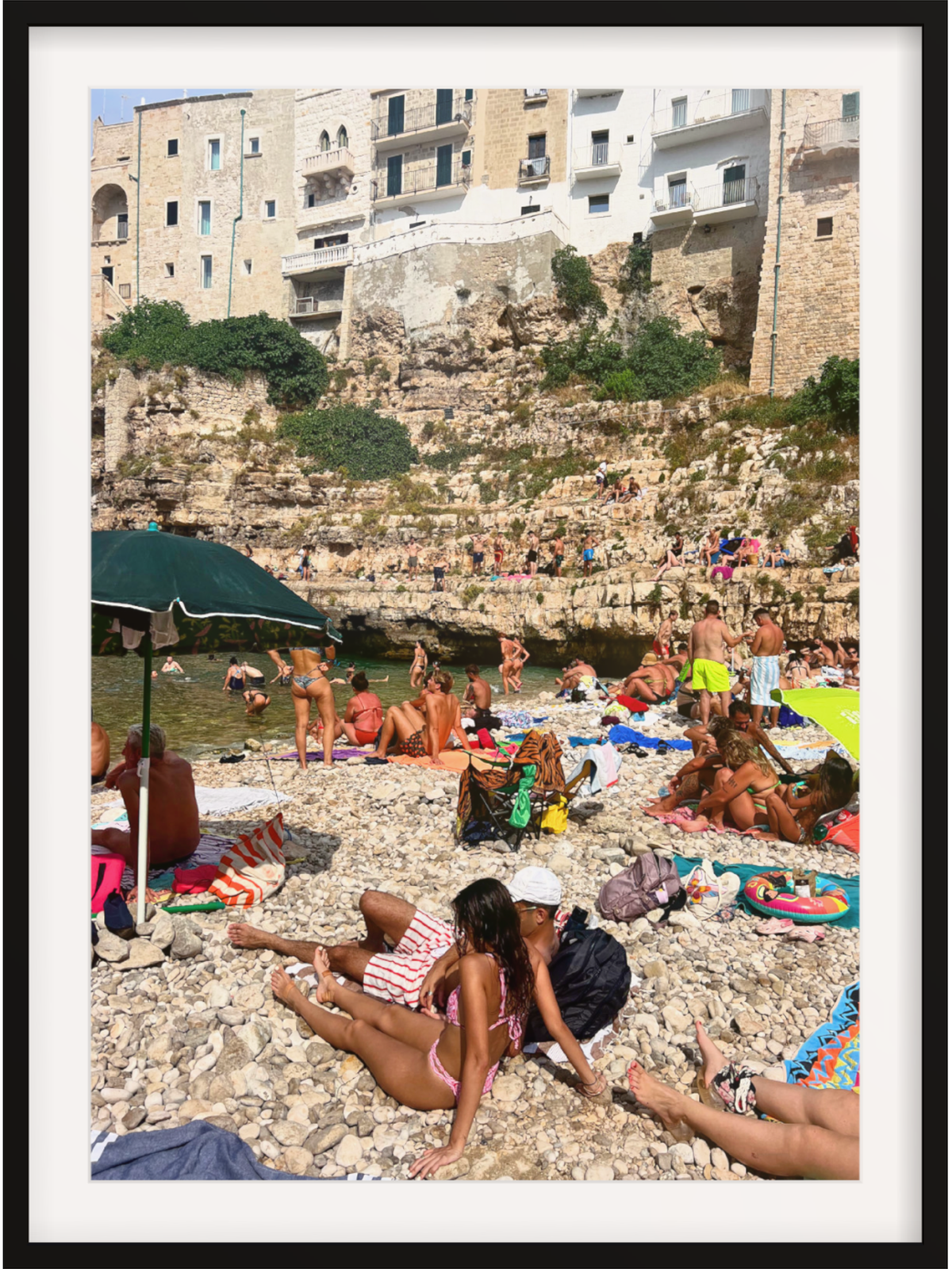Beach scene with people sunbathing on a rocky shore with buildings in the background