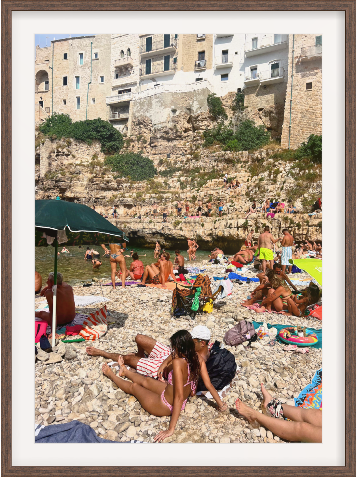 Beach scene with people sunbathing on a rocky shore with buildings in the background