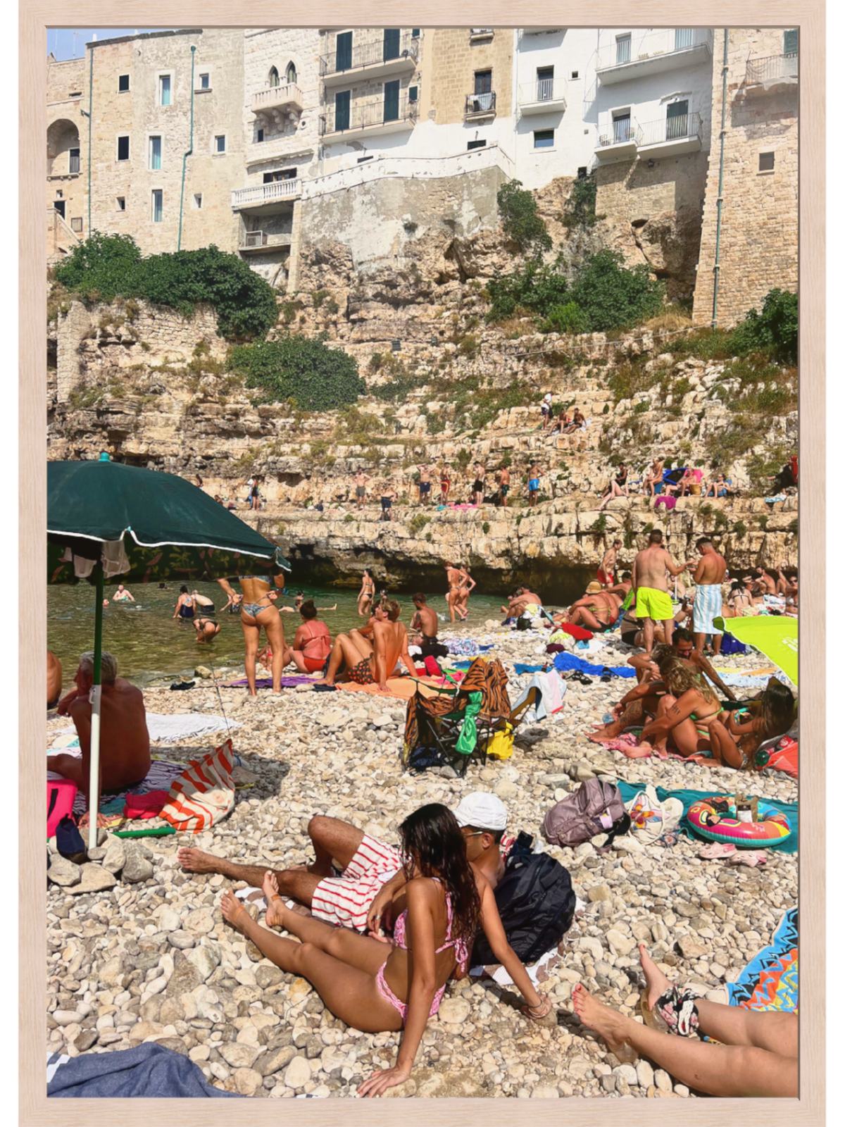 Beach scene with people sunbathing on a pebbly shore, buildings in the background.