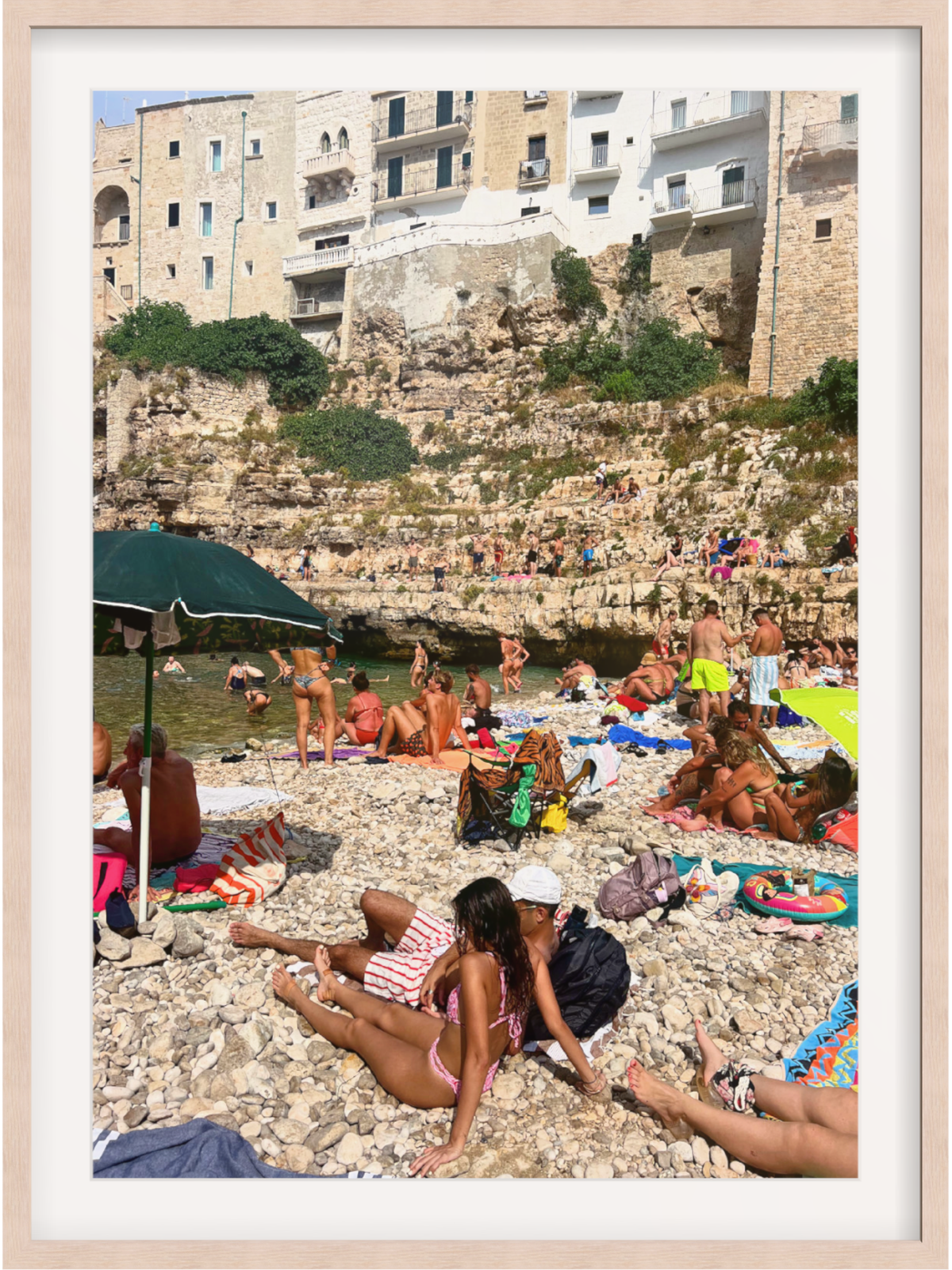 People sunbathing on a rocky beach with buildings in the background