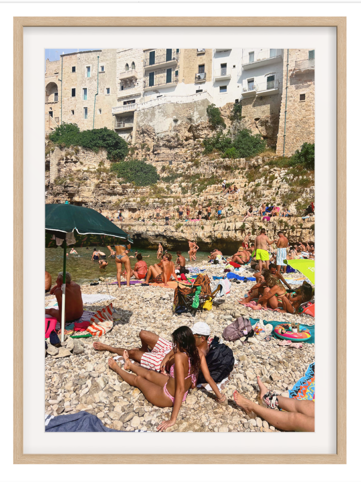 Beach scene with people sunbathing on a rocky shore with buildings in the background.