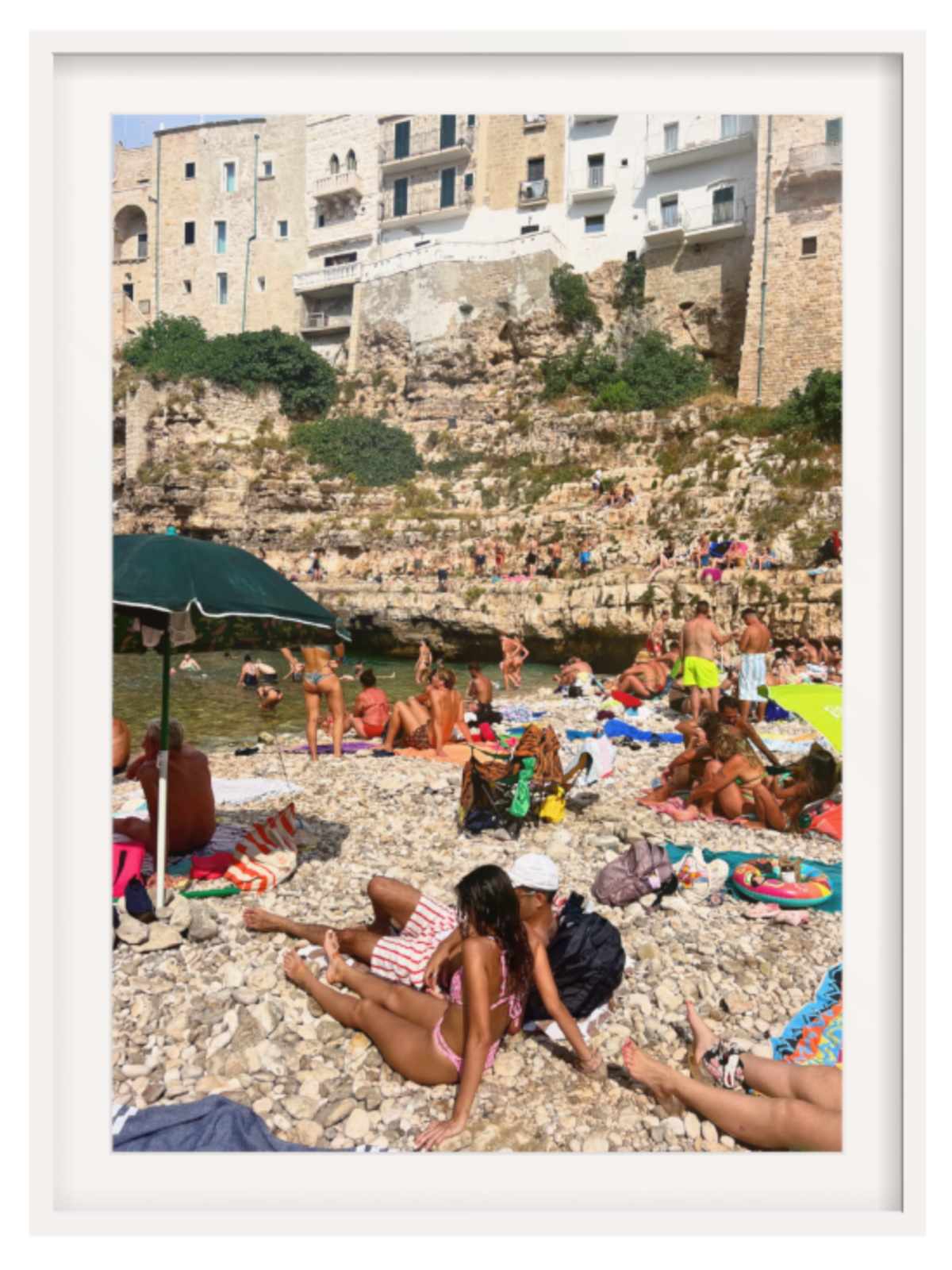People enjoying a sunny day at a rocky beach with buildings in the background.