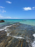 Coastal scene with clear blue sky, turquoise water, and rocky shoreline.
