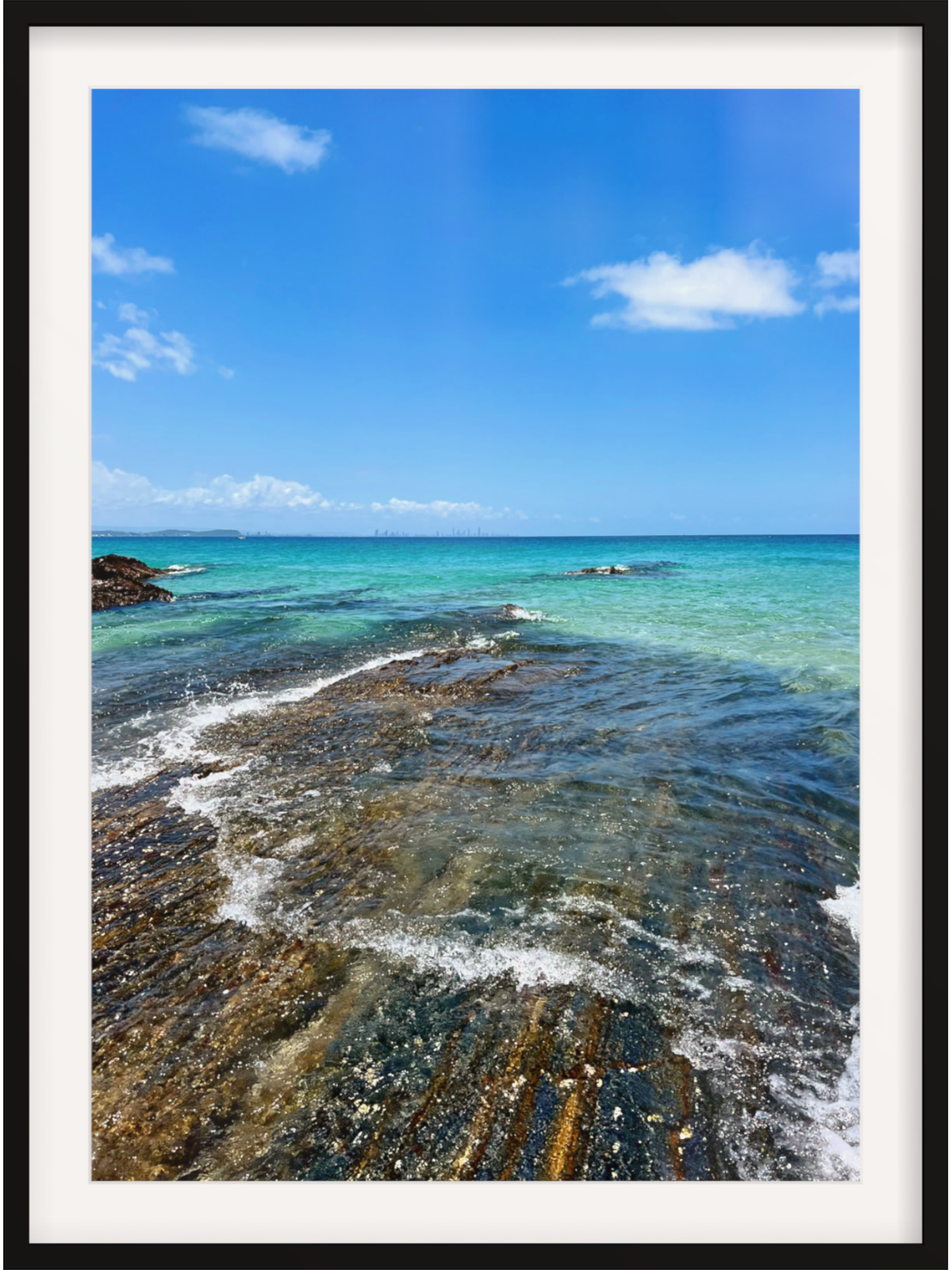 Coastal scene with clear blue water and rocky shoreline under a bright sky.
